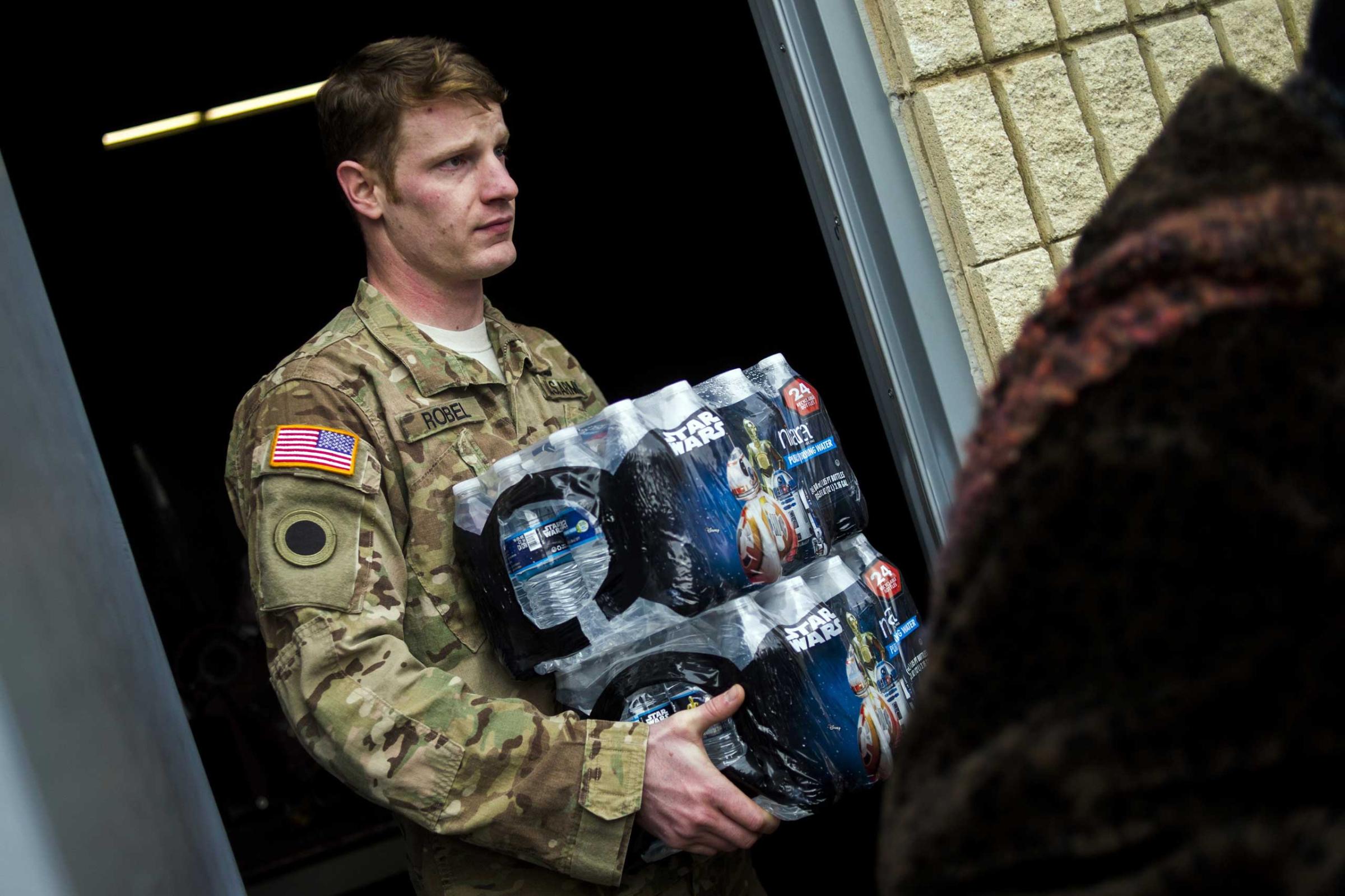 Michigan National Guard Staff Sgt. Stephen Robel helps carry a case of water to the vehicle of Flint resident Karand Houston as the first seven Michigan National Guard soldiers arrive on the ground at fire stations on Jan. 13, 2015 throughout Flint, assigned by Gov. Rick Snyder on Tuesday to help distribute water and relieve residents in relation to the Flint water crisis. Safe drinking water has not flowed from many Flint faucets for almost two years after the state-run city switched its source to the highly corrosive Flint River and failed to treat it properly to protect lead from leaching into it.
