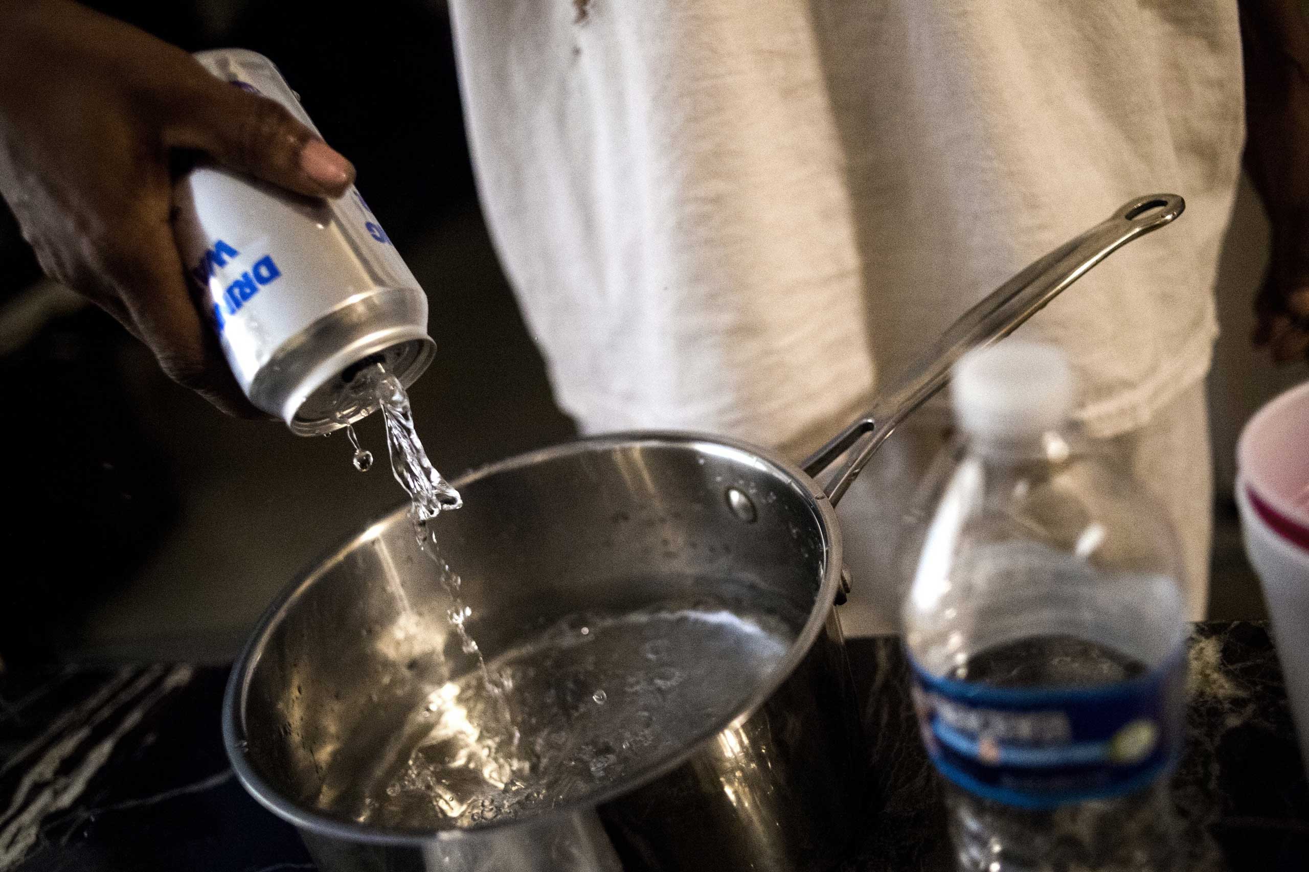 Flint resident Lorraine Jones pours canned water into a pot in preparation for boiling to cook on Jan. 19, 2016, at River Park Apartments in Flint, Mich.