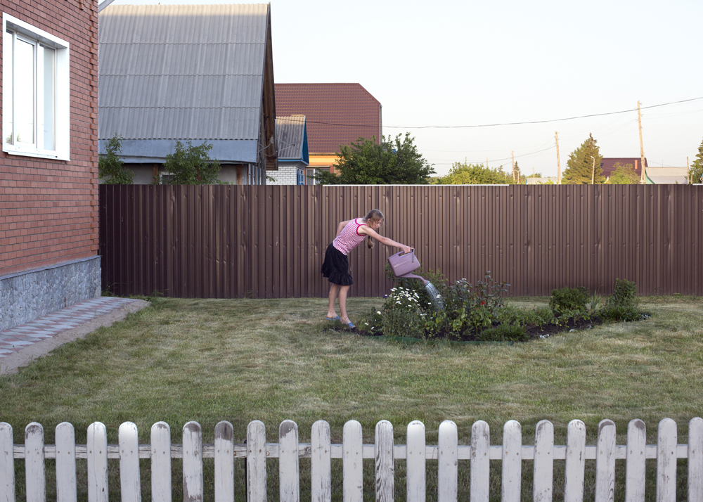 A girl waters plants in the front yard of a new house purchased by her parents three days ago in Solnzevka, Russia, 2014.