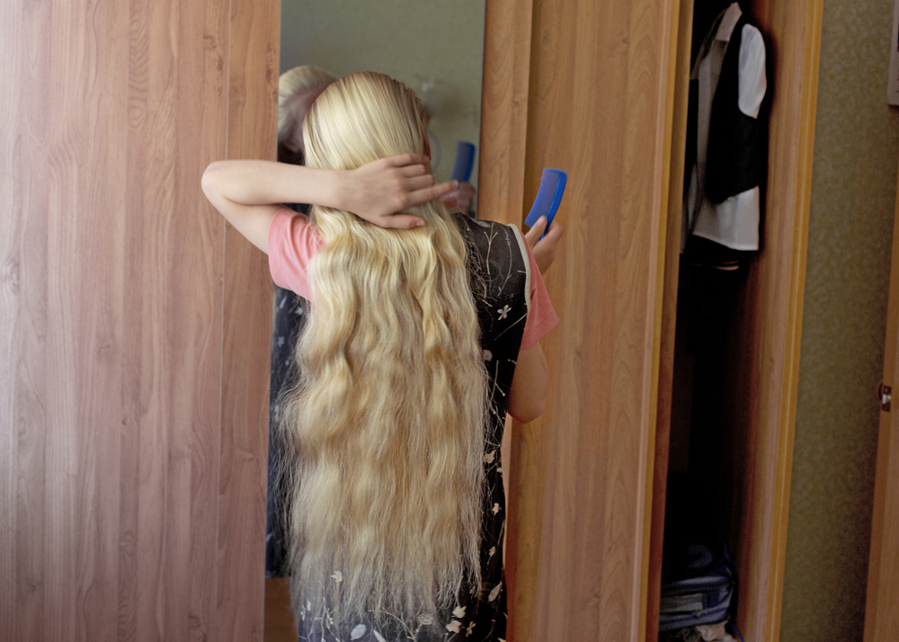 An eleven-year-old girl braiding her hair before church service in Petrovka, Russia, 2014.