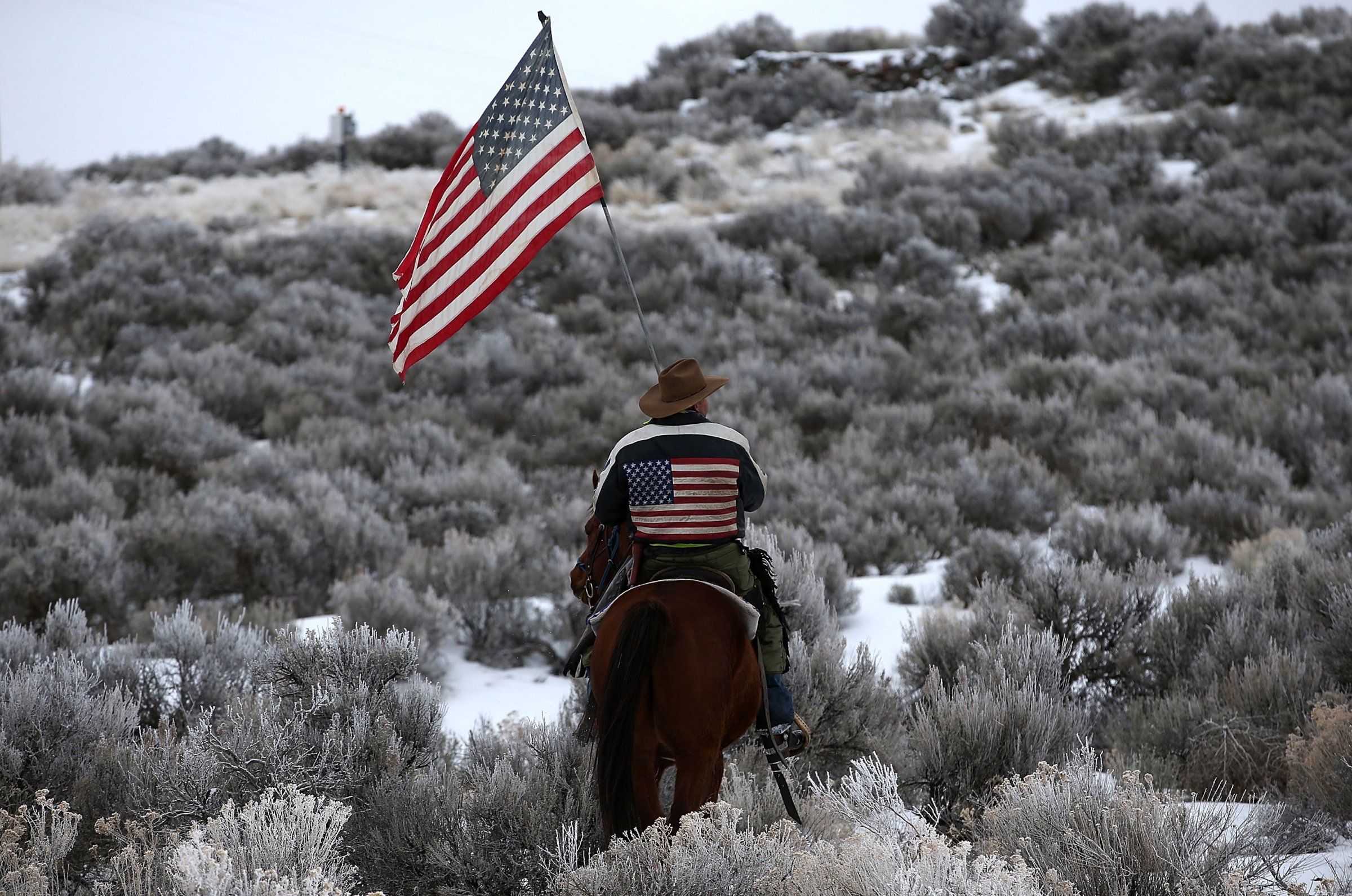 Dwayne Ehmer carries an American flag as he rides his horse on the Malheur National Wildlife Refuge near Burns, Ore., on Jan. 7, 2016.