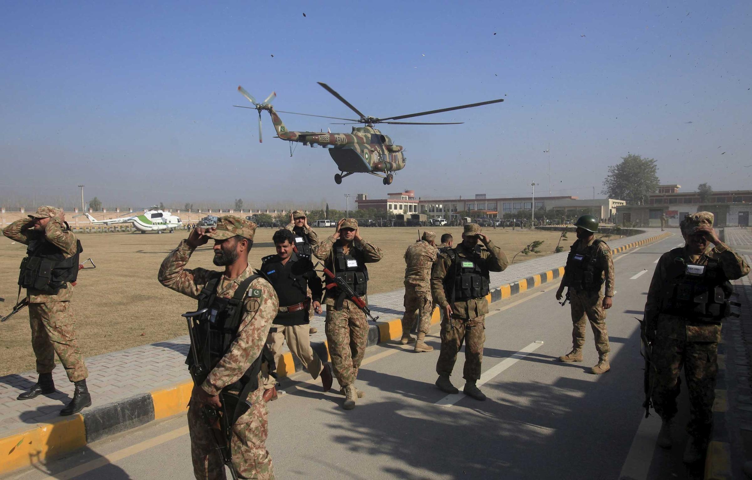Soldiers holds their caps as a helicopter flies past during an operation, after a militant attack at Bacha Khan University in Charsadda, Pakistan, Jan. 20, 2016.