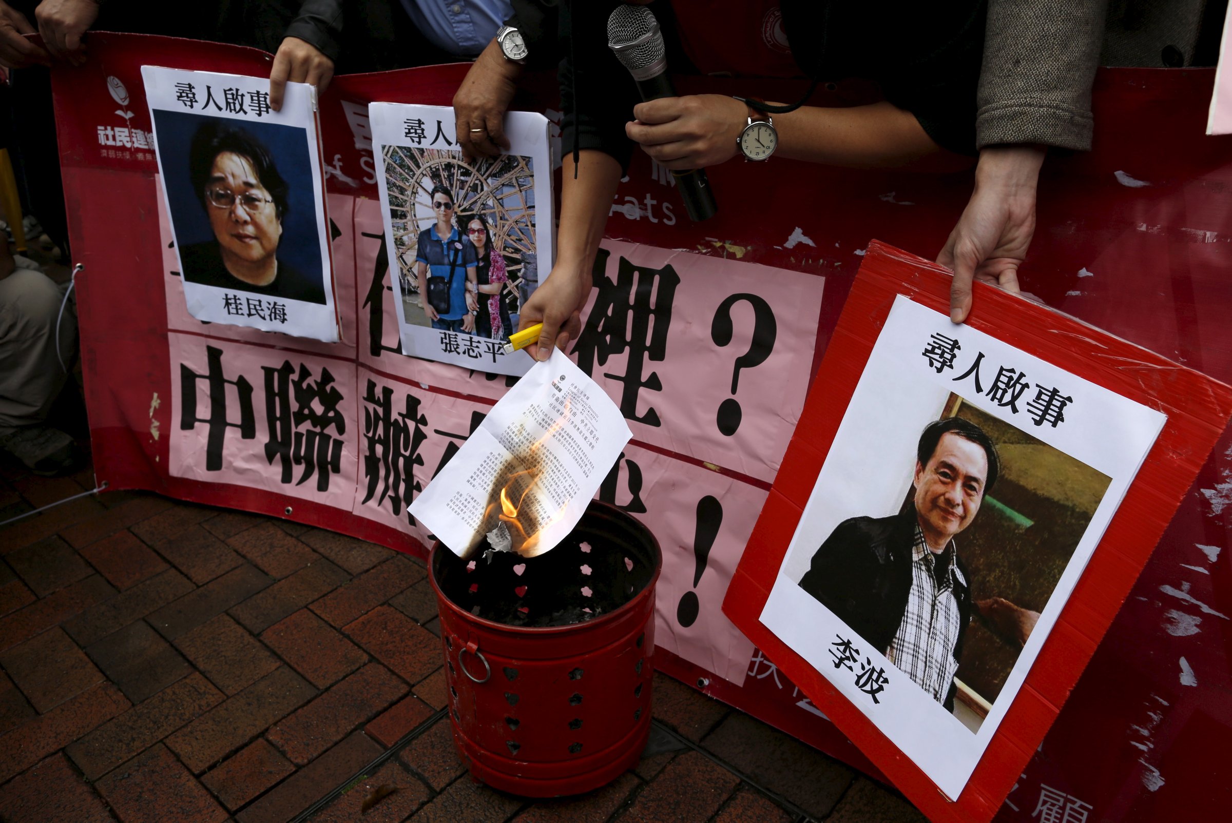 A pro-democracy demonstrator burns a letter next to pictures of missing staff members of a publishing house and a bookstore during a protest to call for an investigation behind their disappearance, outside the Chinese liaison office in Hong Kong