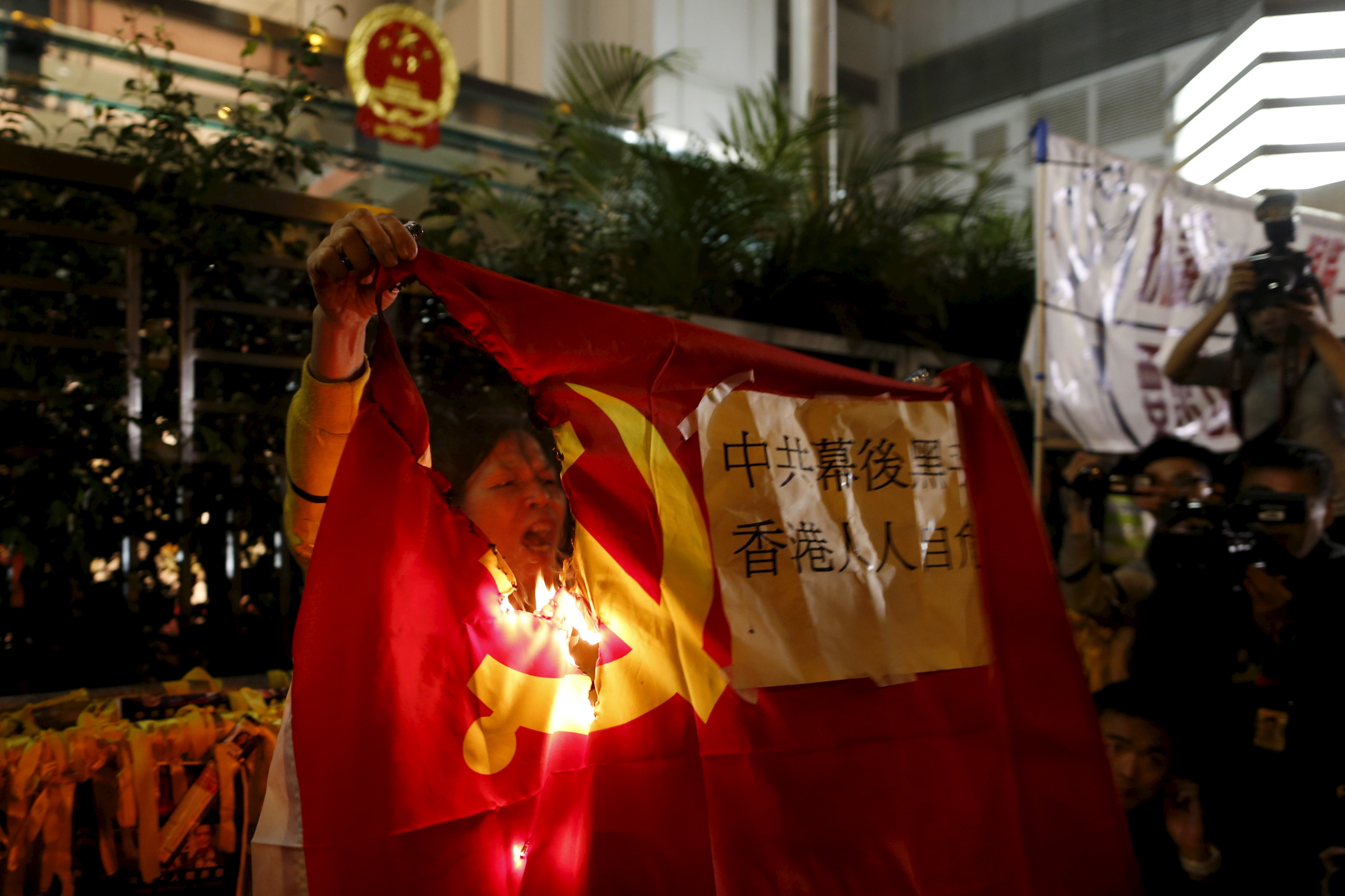 A demonstrator burns a flag of the Communist Party of China during a protest over the disappearance of booksellers, outside the Chinese liaison office in Hong Kong, China