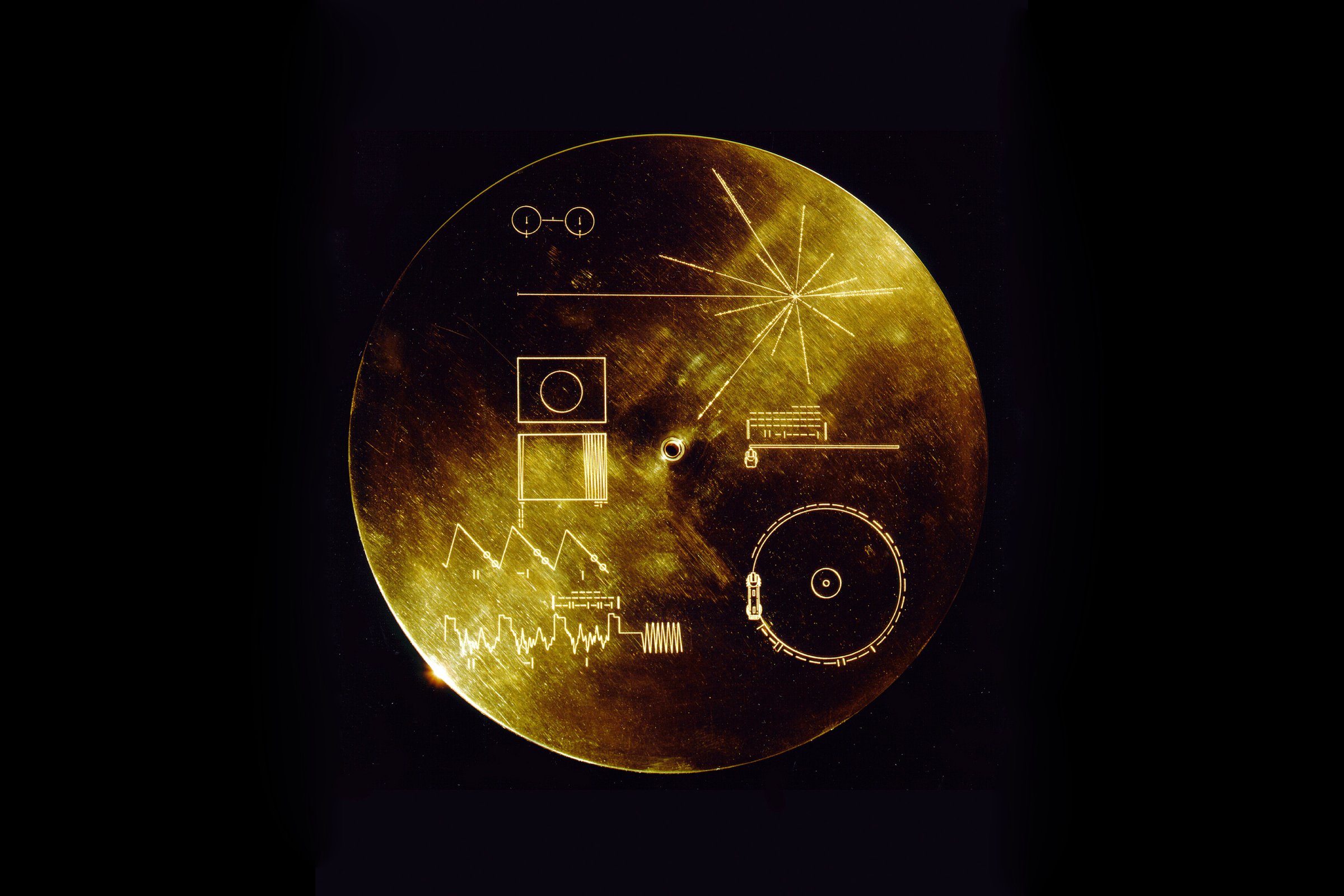 This gold aluminum cover was designed to protect the Voyager 1 and 2 'Sounds of Earth' gold-plated record from micrometeorite bombardment, but also serves a double purpose in providing the finder a key to playing the record. The explanatory diagram appears on both the inner and outer surfaces of the cover, as the outer diagram will be eroded in time. Flying aboard Voyagers 1 and 2 are identical golden records, carrying the story of Earth far into deep space. The 12 inch gold-plated copper discs contain greetings in 60 languages, samples of music from different cultures and eras, and natural and man-made sounds from Earth.