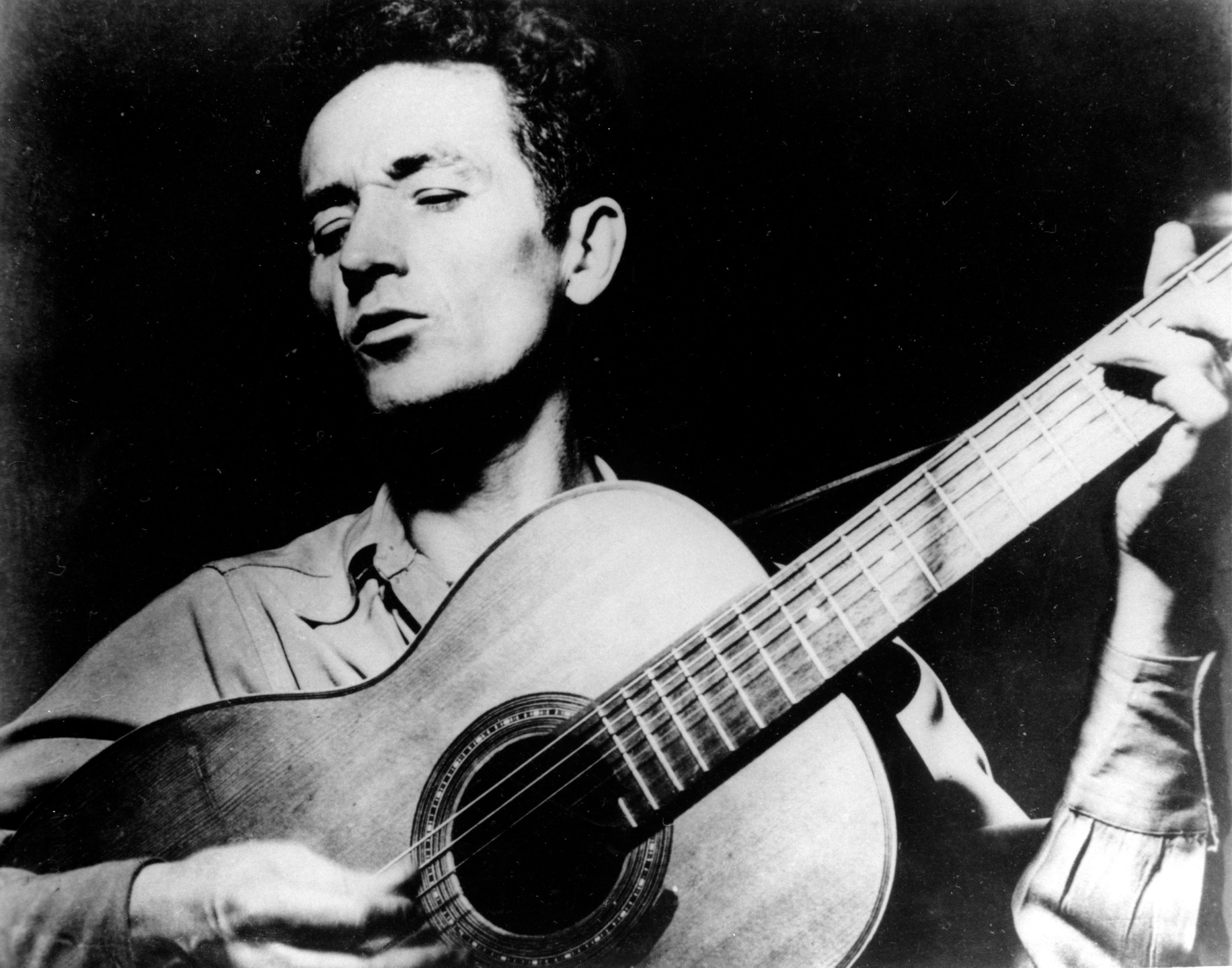 Folk singer, Woody Guthrie, singing a song and playing his guitar.