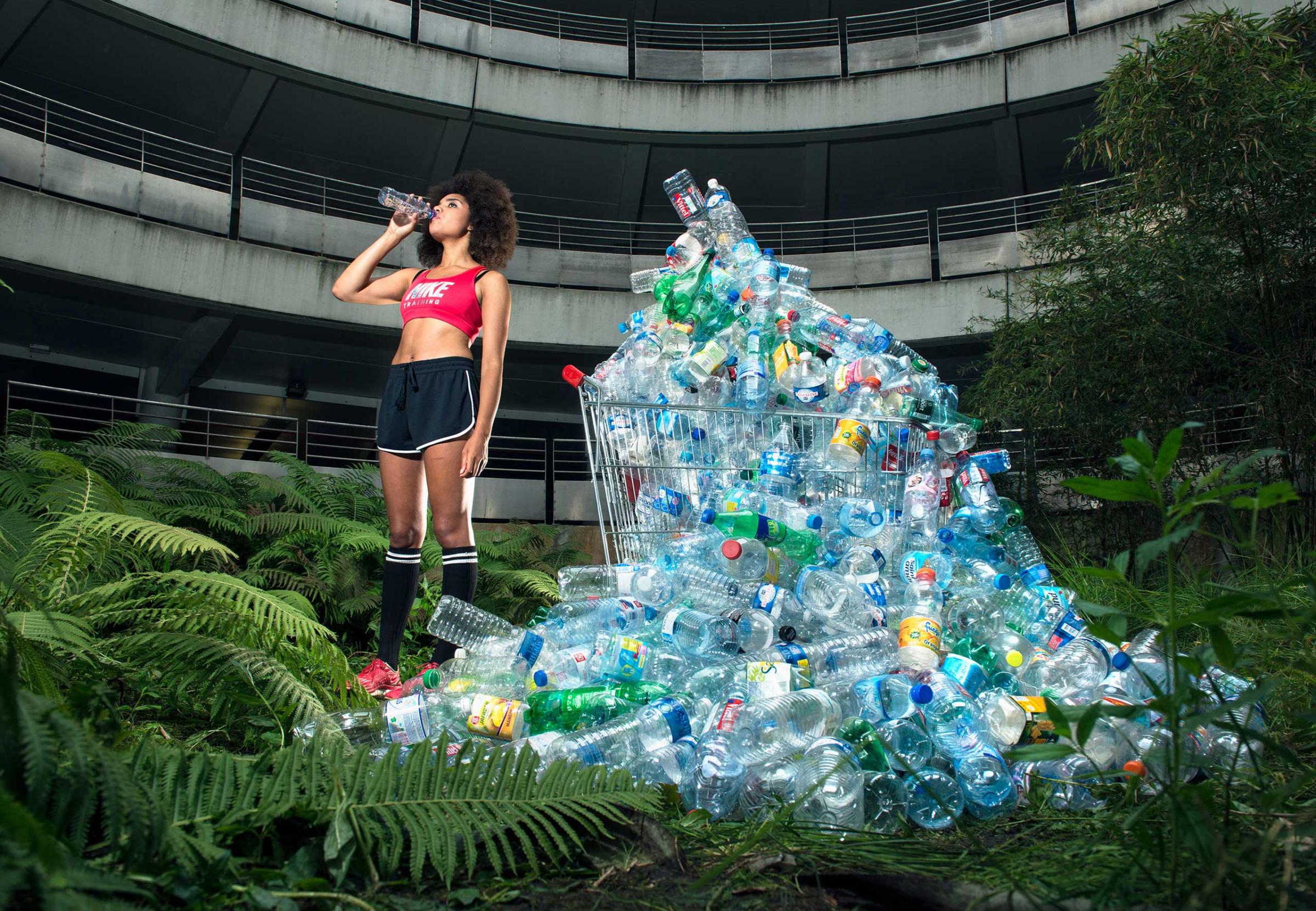 A woman drinks out of a water bottle near a "waste bank" of recycled waste in France. It's part of an exhibition exploring the excessive waste habits.