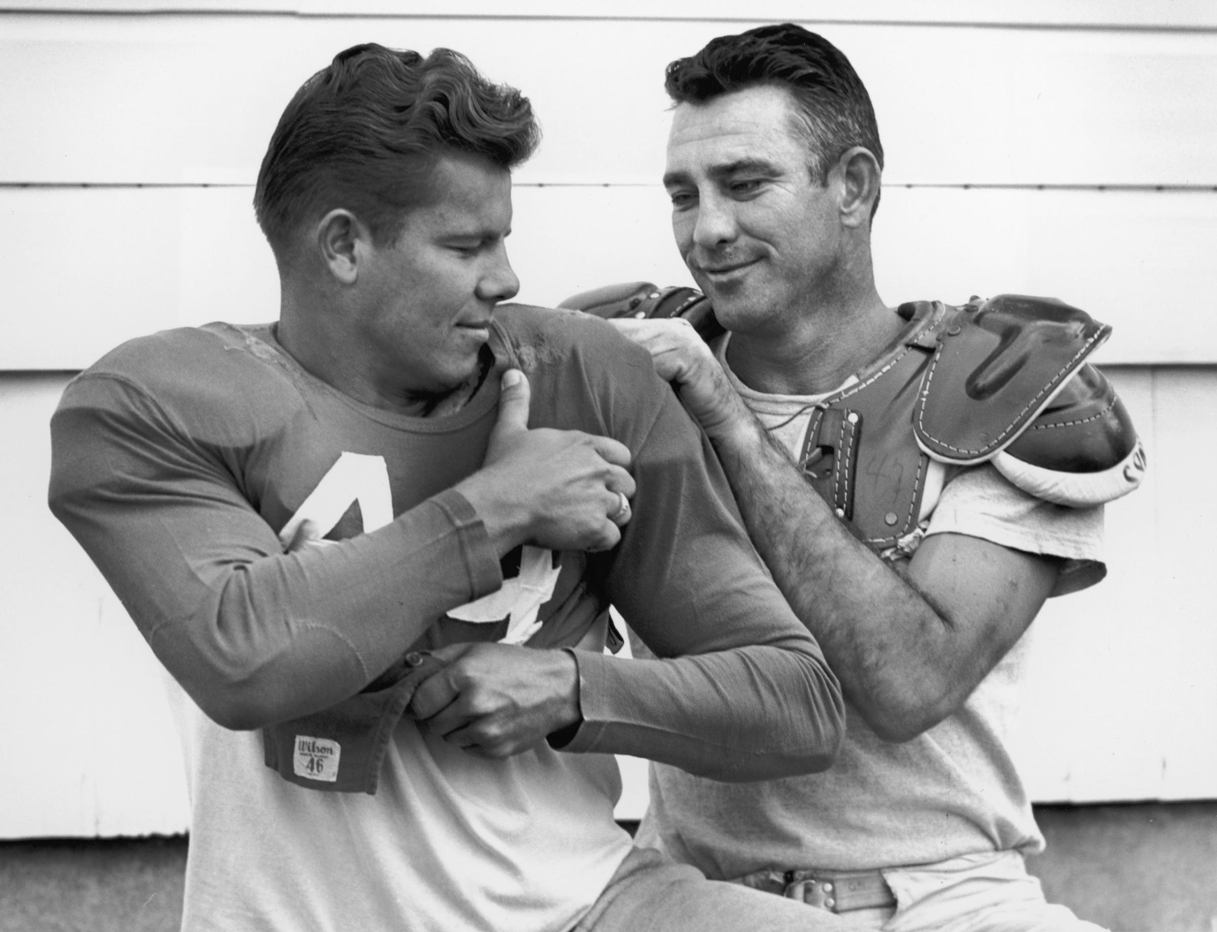 Football player Charlie Conerly (right), quarterback for the New York Giants, attempts to assist his teammate, halfback Kyle Rote, by untangling the back of his jersey that has gotten caught in his shoulder pad, circa 1950s.