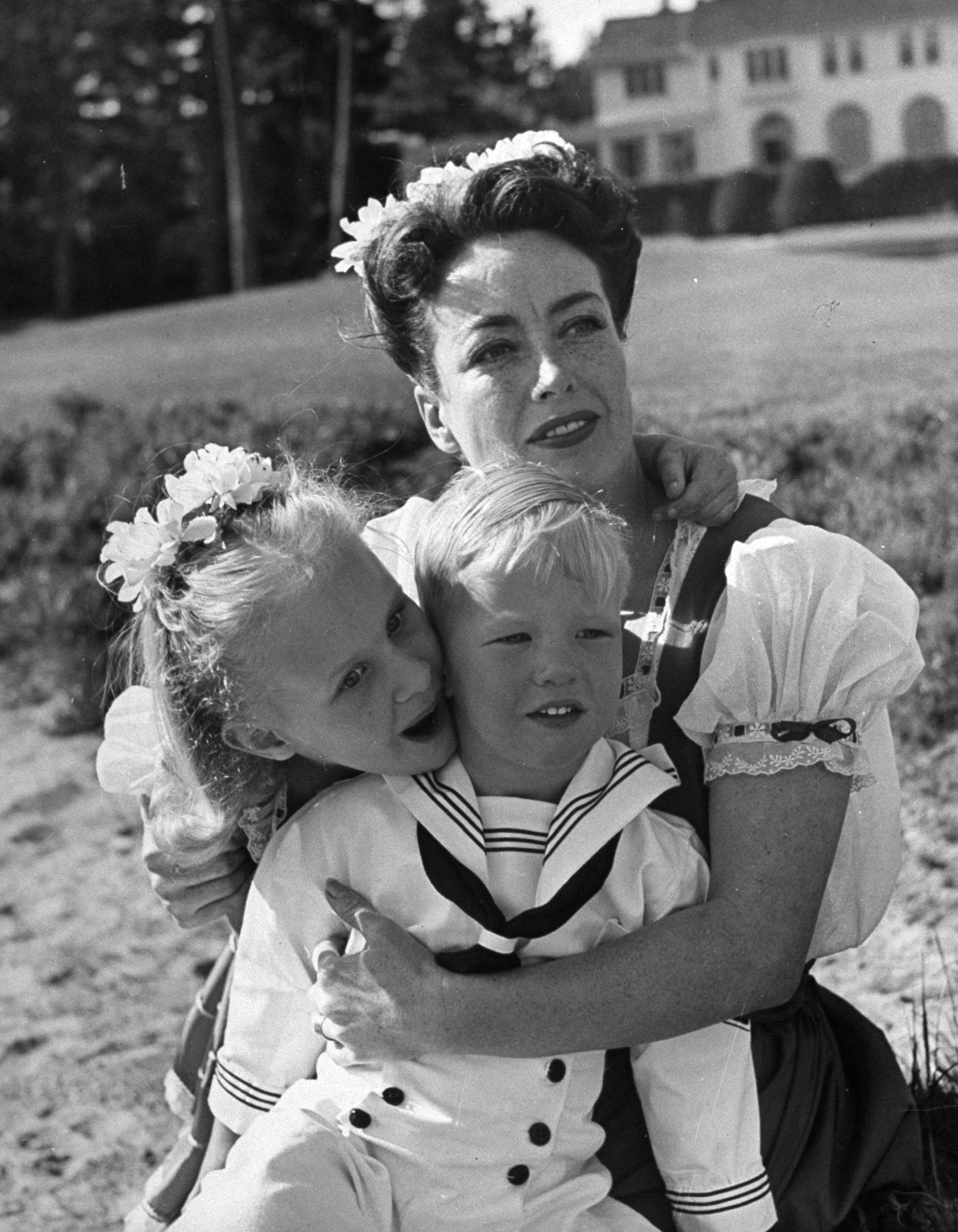 Joan Crawford hugging her two adopted children, Christina and Christopher, while sitting on beach, 1945.