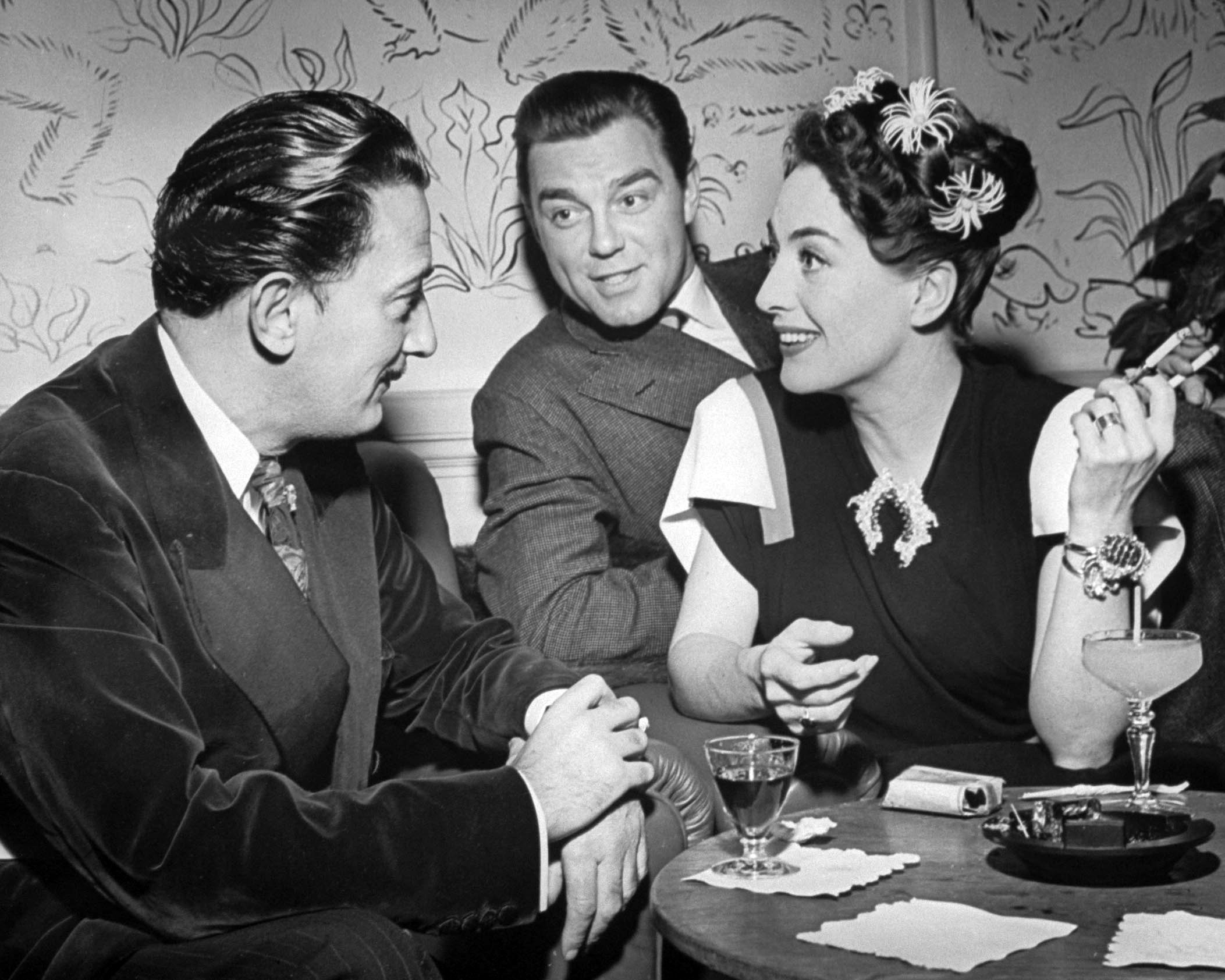 Joan Crawford chatting with artist Salvador Dali as her husband Phillip Terry looks on at the Del Monte resort. 1945.