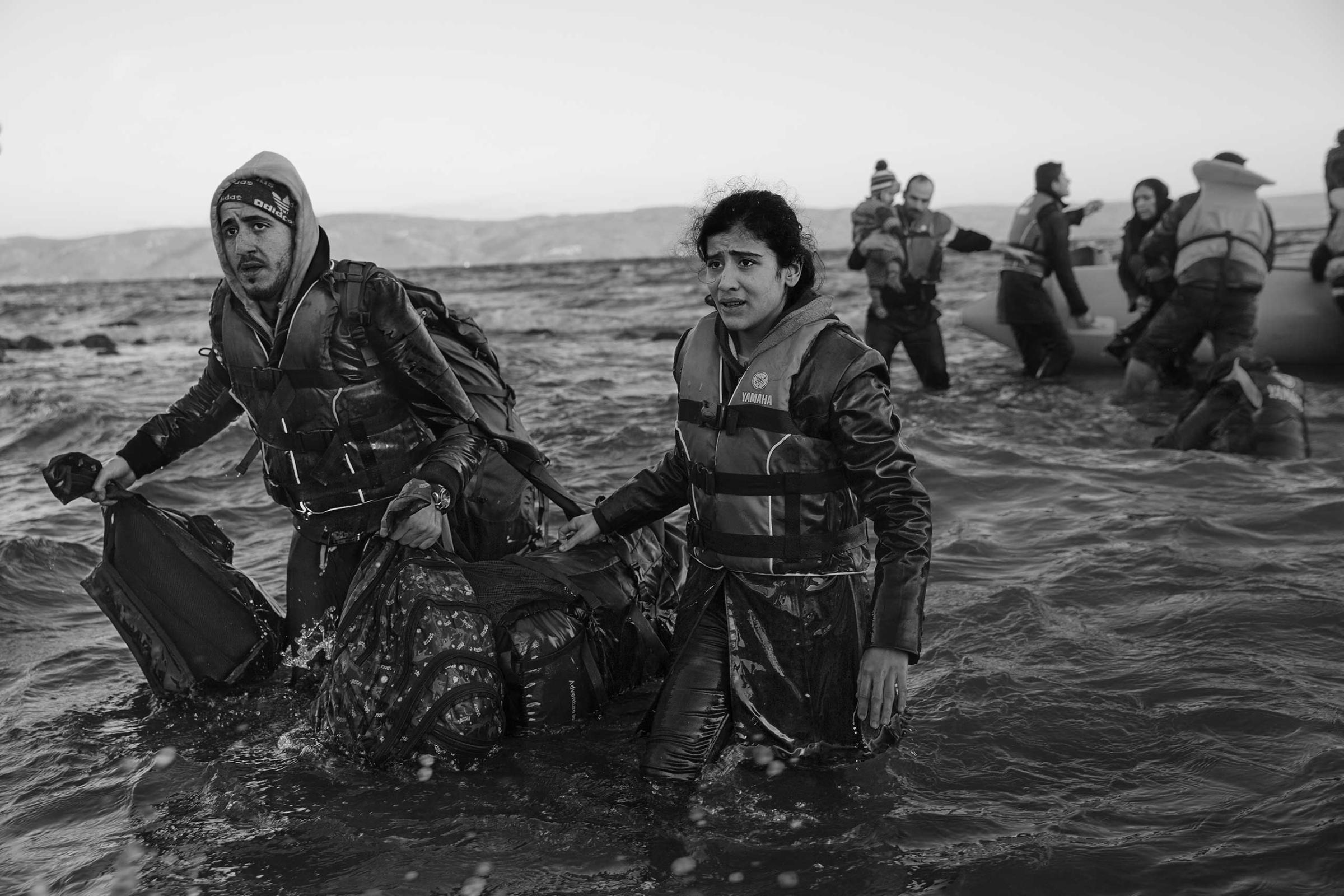 A man and woman carry their belongings to Lesbos after their inflatable boat became stuck on the rocks about 160 feet from the Greek shore.