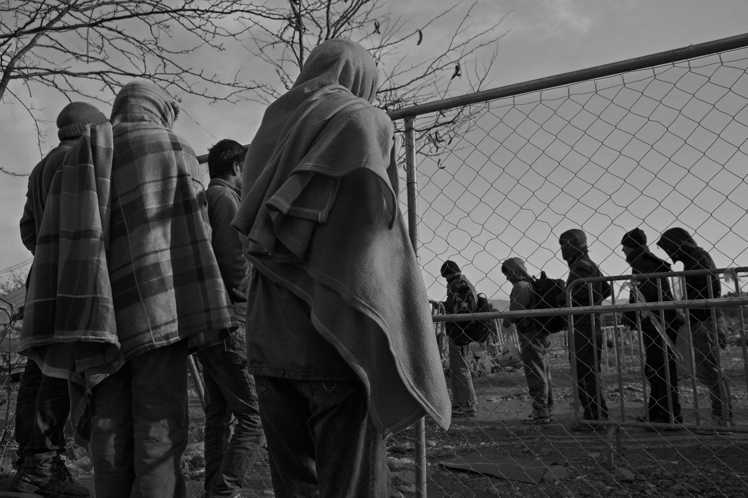 Refugees and migrants from Morocco, Iran, Pakistan, Bangladesh, and Somalia, who are not permitted to cross from Greece into Macedonia, watch as those from war-torn countries of Afghanistan, Iraq and Syria, pass into Macedonia.