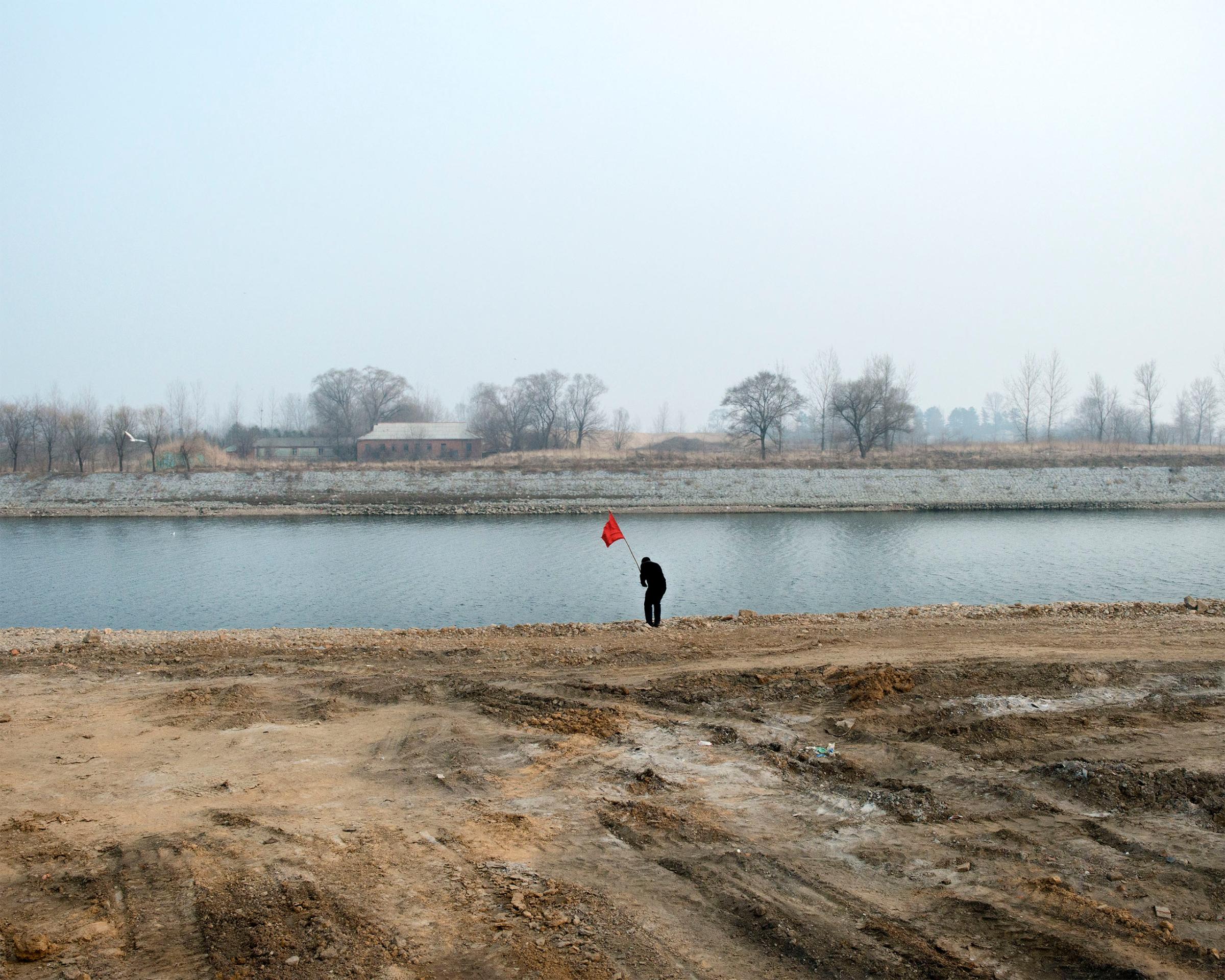 A man places a red flag at the river bank across from north korea border in Dandong, China.