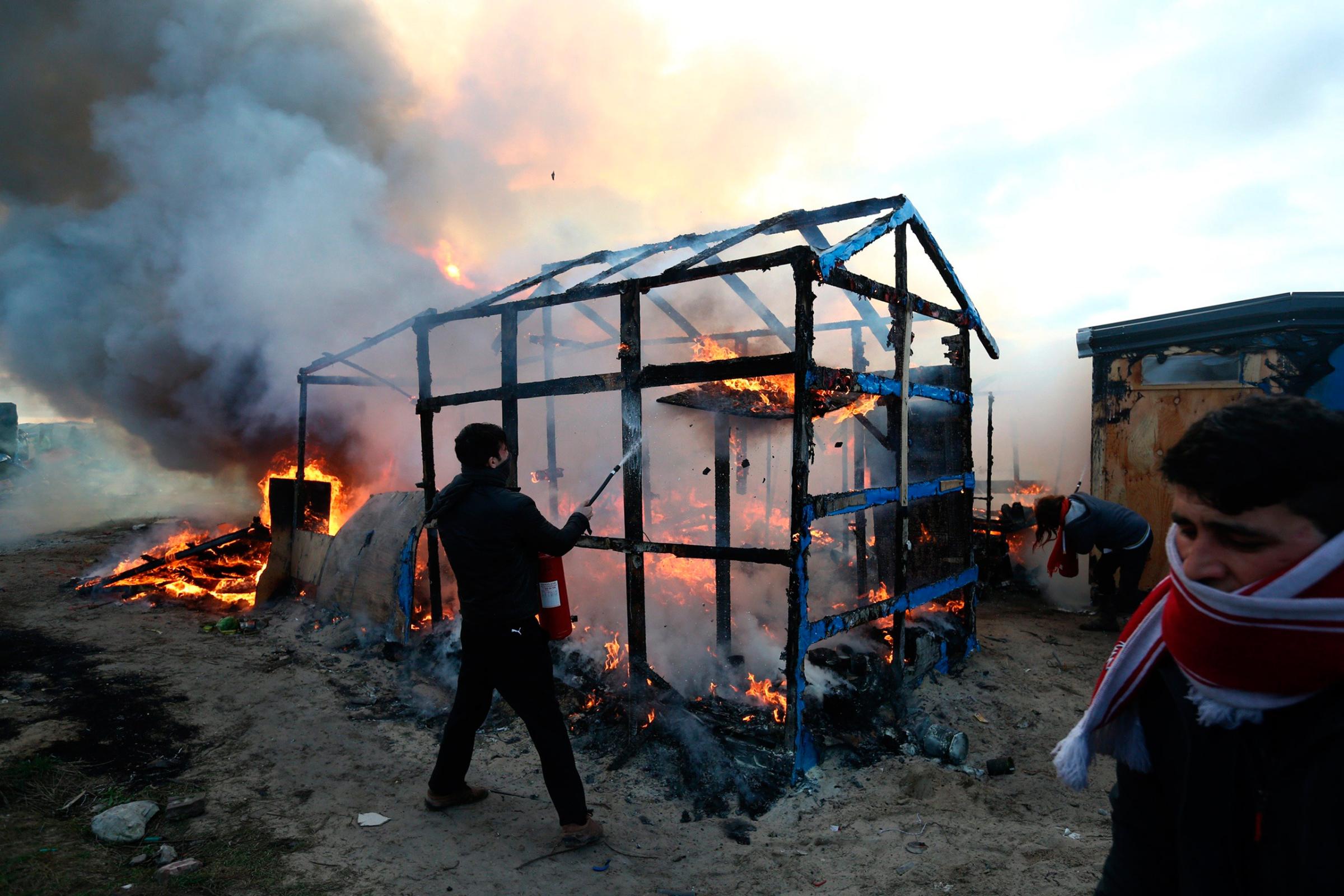 A migrant attempts to extinguish a fire as a shelter burns as police officers clear part of the "Jungle" migrant camp in Calais, France, Feb. 29, 2016.