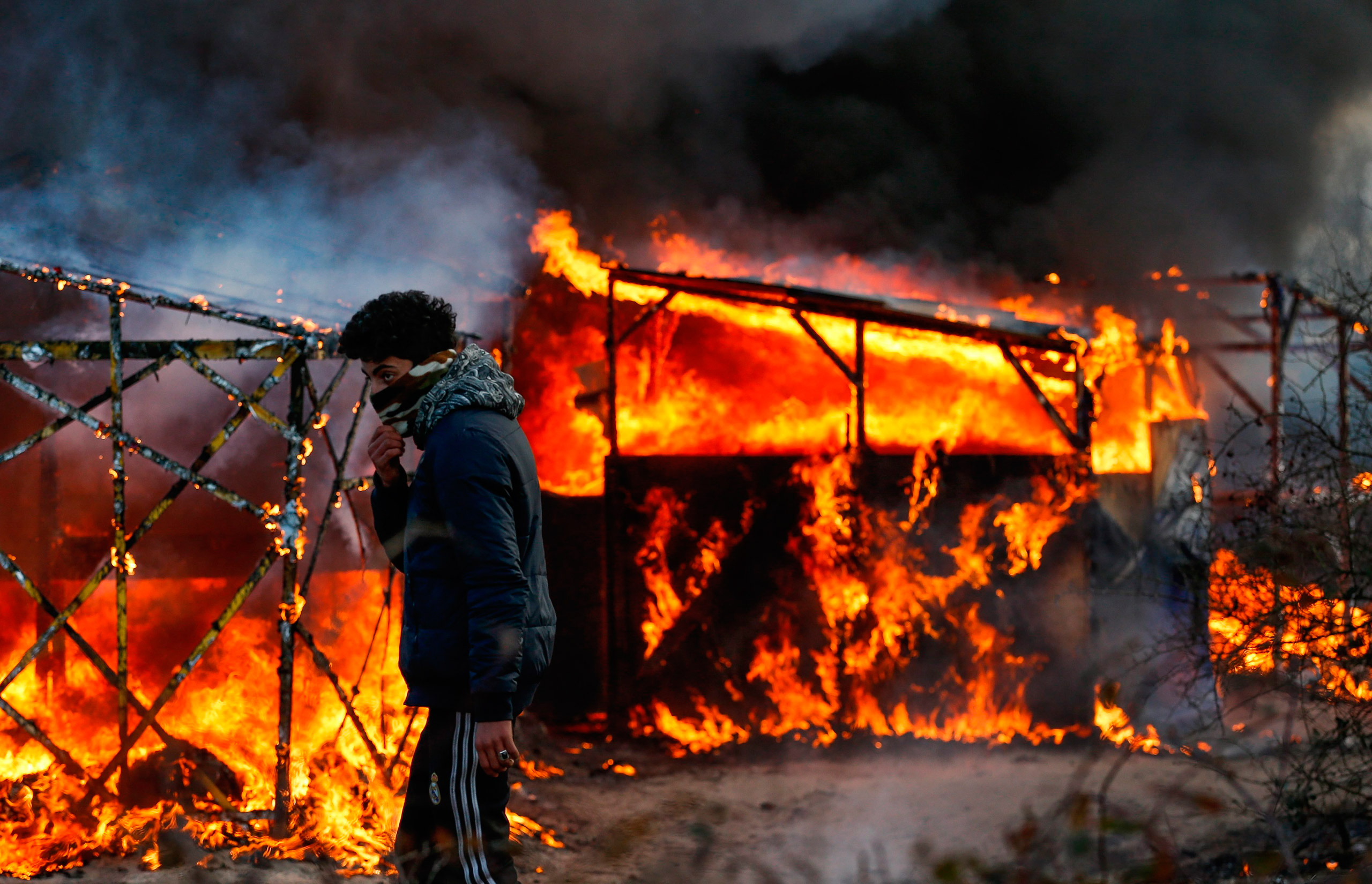 A refugee watches a shelter burn during the start of the expulsion of a part of the  Jungle  migrant camp in Calais, France, Feb. 29, 2016.