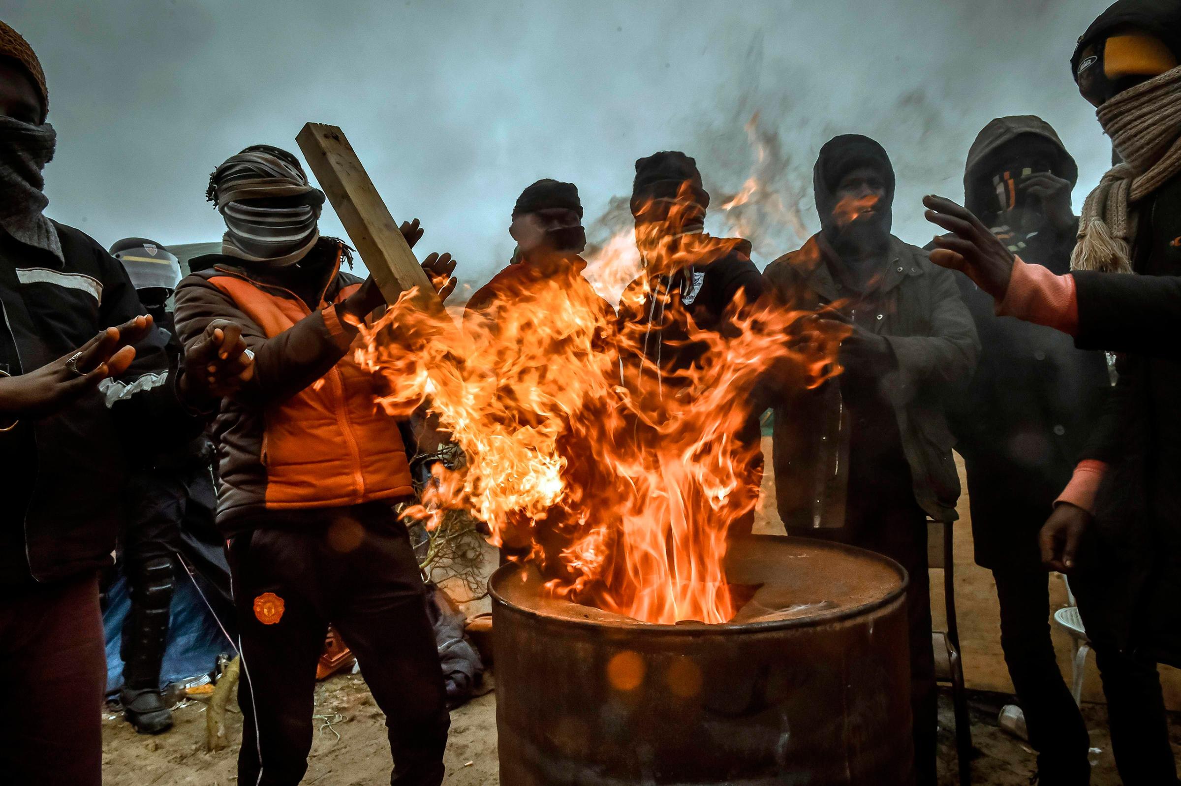 Migrants keep warm around a fire in a trash can as authorities dismantle shacks in the "Jungle" camp in Calais, France, March 1, 2016.