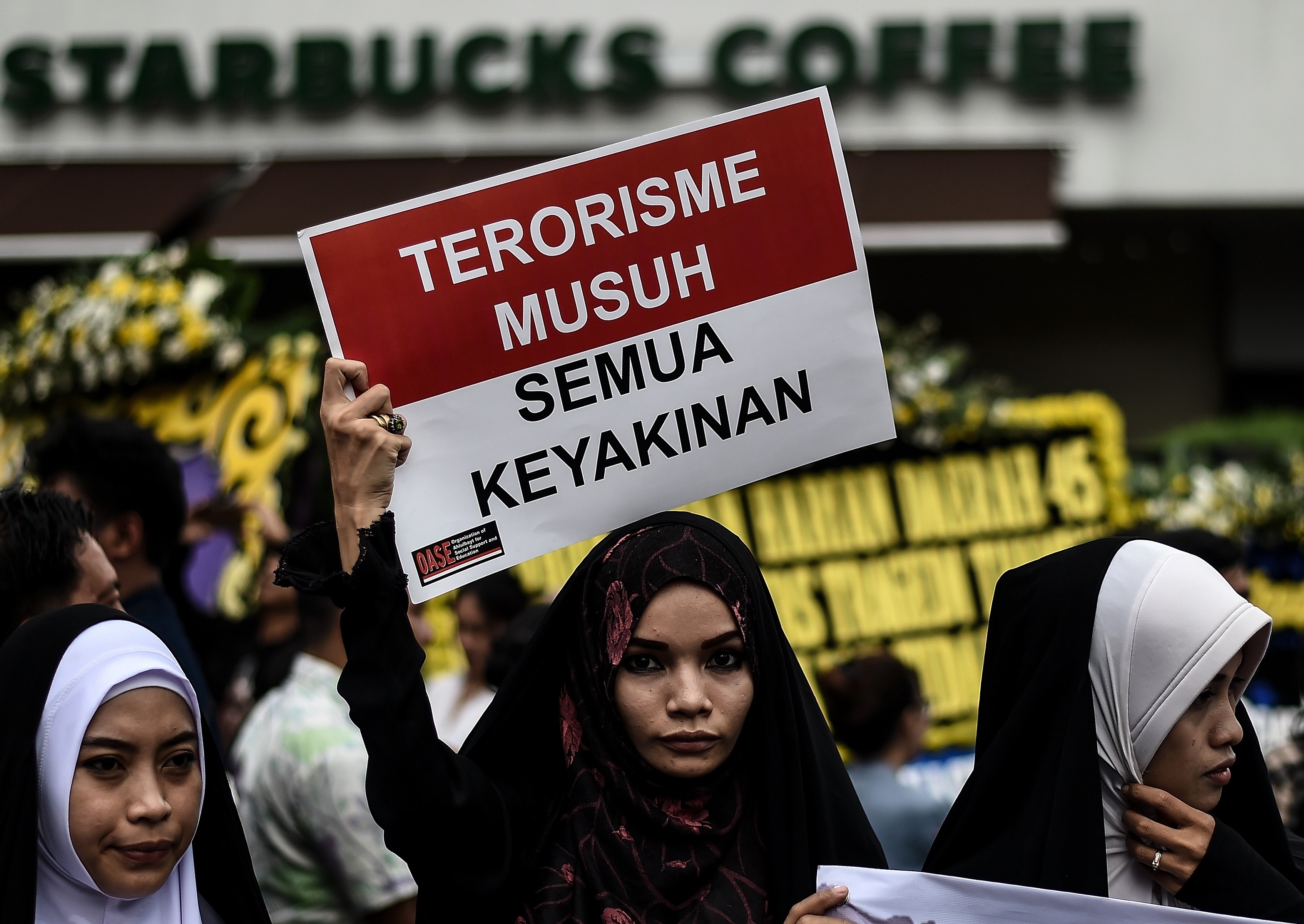 Women hold placards during a vigil outside the damaged Starbucks coffee shop in central Jakarta on Jan. 15, 2016, a day after a series of explosions hit the Indonesian capital (Manan Vatsyayana—AFP/Getty Images)