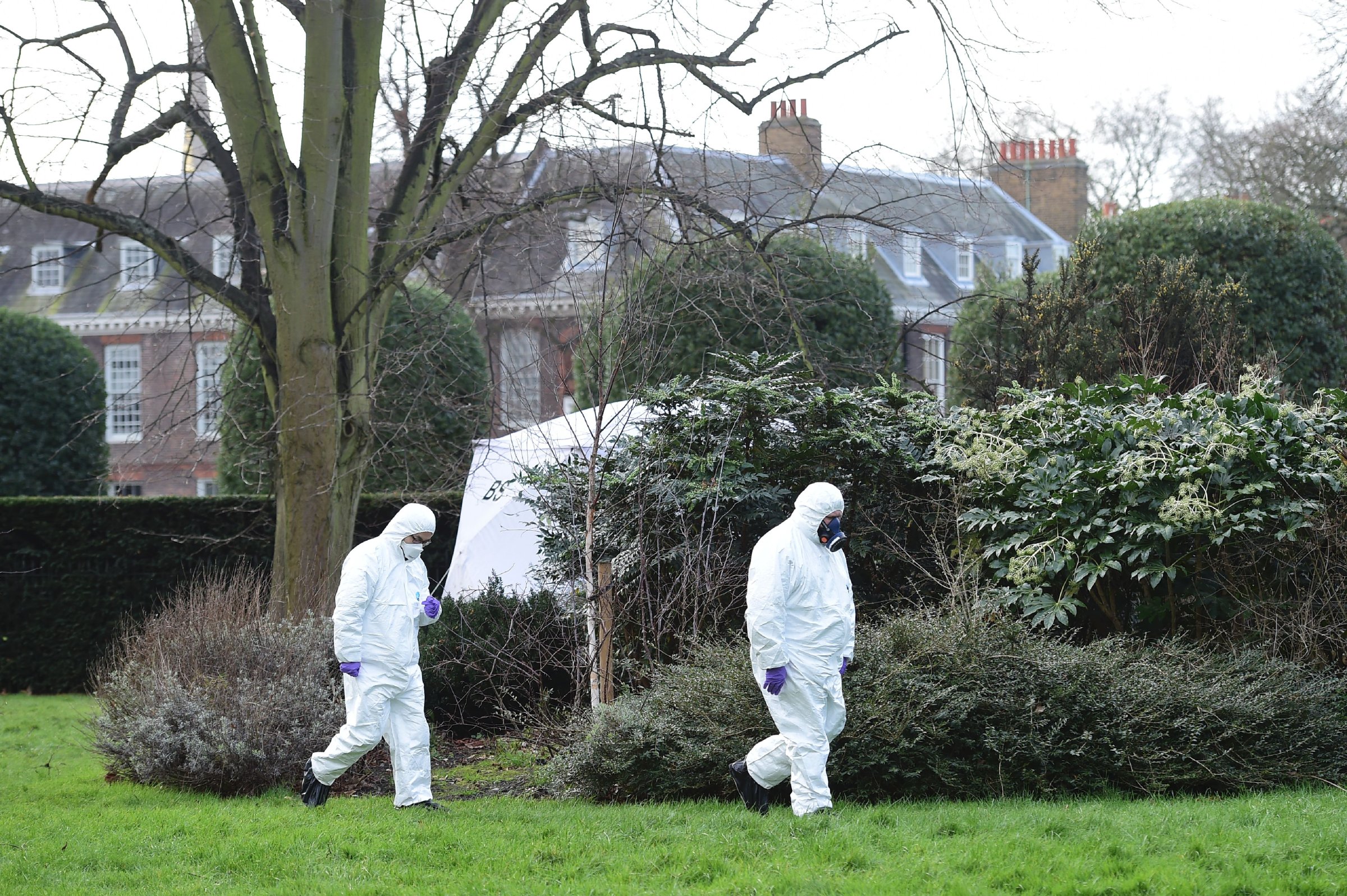 Forensics officers in overalls and masks walk by the tent errected over the scene where a man died after being discovered on fire in the park outside the wall of Kensington Palace in London on Feb. 9, 2016.