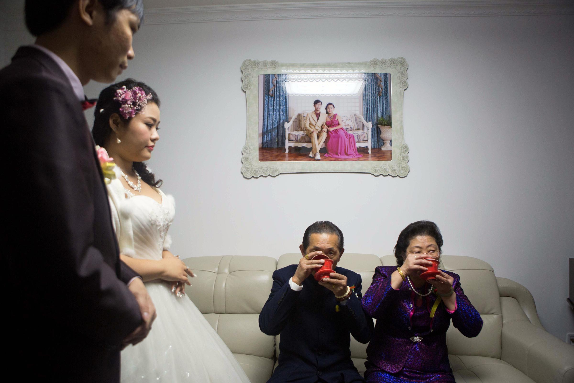 Xia Jiachen and Xu Chuyun, at left, honor the groom's grandparents during their wedding in November 2015. Pre-wedding photos are displayed on the wall.