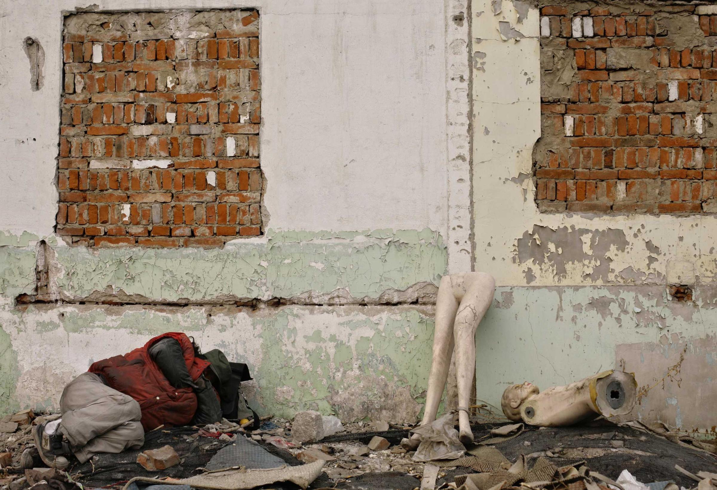A man sleeps next to pieces of mannequins amongst the rubble of a demolished house in Beijing, Dec. 26, 2007.