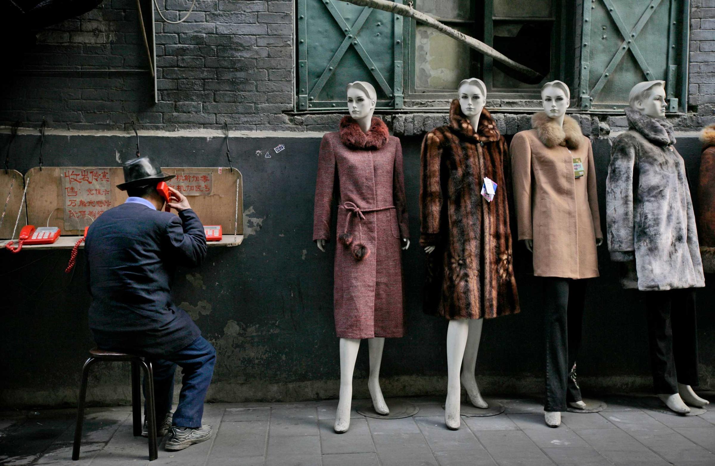 A man speaks on a pay phone next to a clothing shop at a market in Beijing, Wednesday, Dec. 26, 2007.