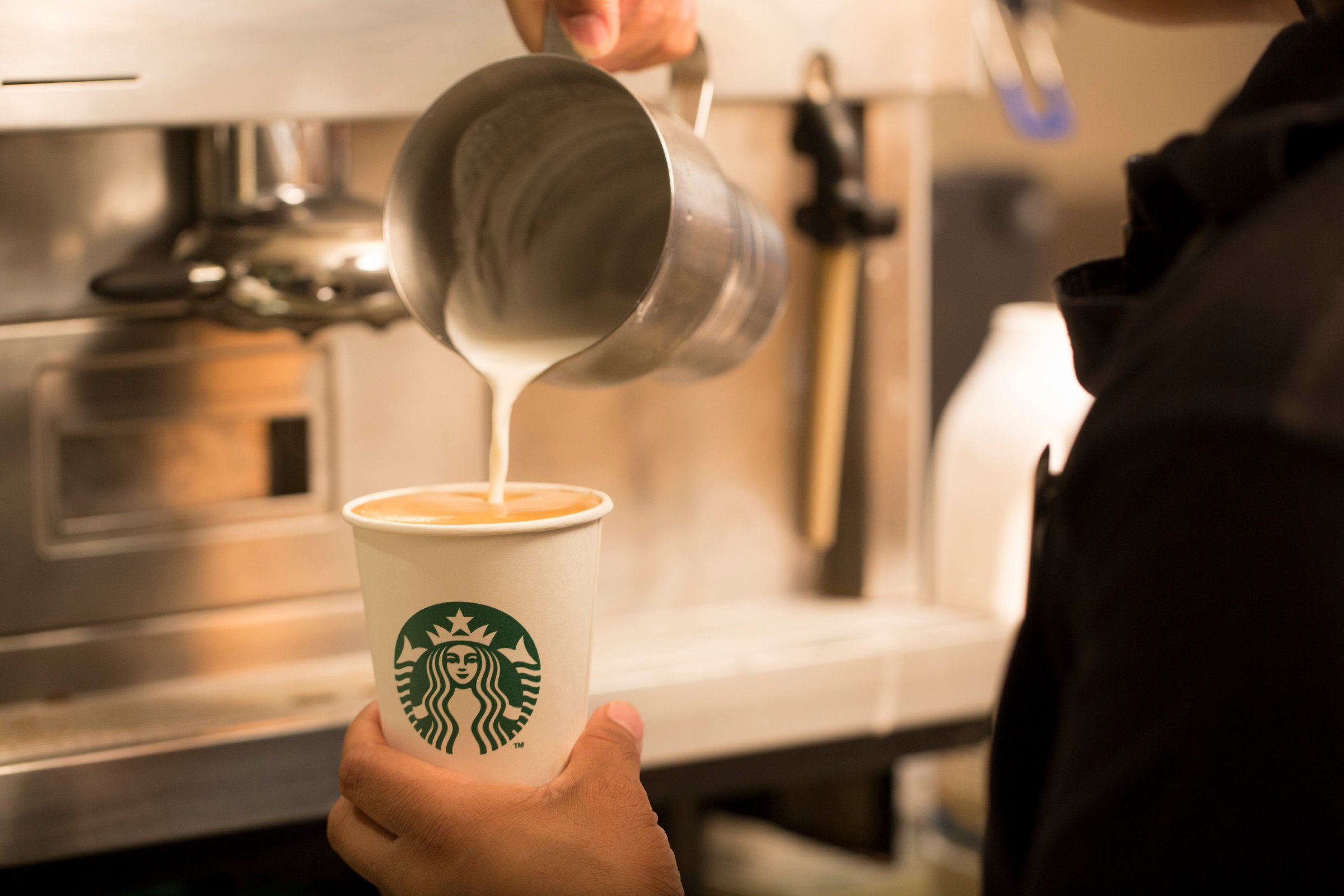 An employee pours milk into a cardboard coffee cup inside a Starbucks Corp. coffee shop in London, U.K., on Monday, Jun. 9, 2014.
