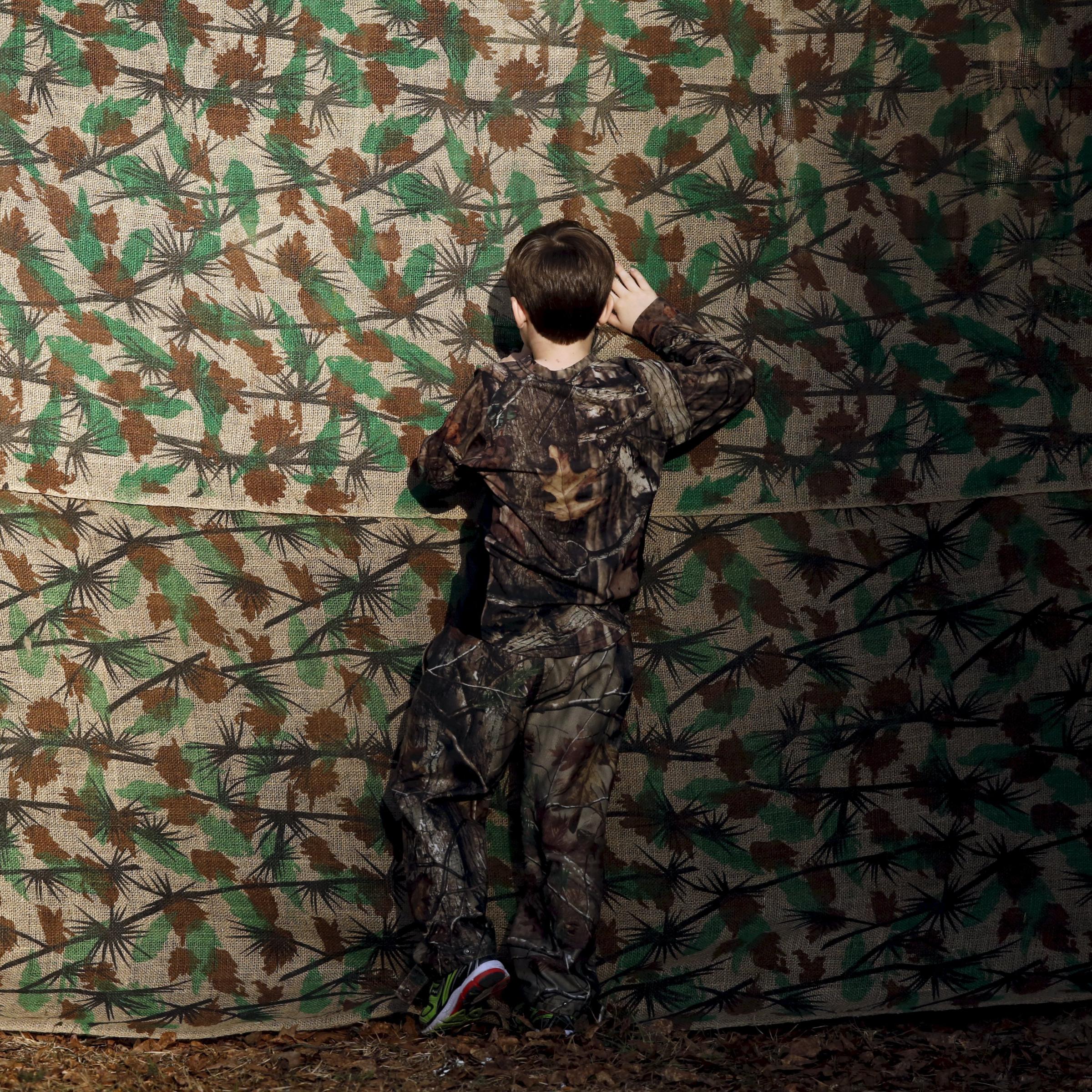 A young boy in camouflage clothing looks through a cloth backdrop to get a glimpse of U.S. Republican presidential candidate Donald Trump at a rally in Walterboro, S.C. on Feb. 17, 2016.