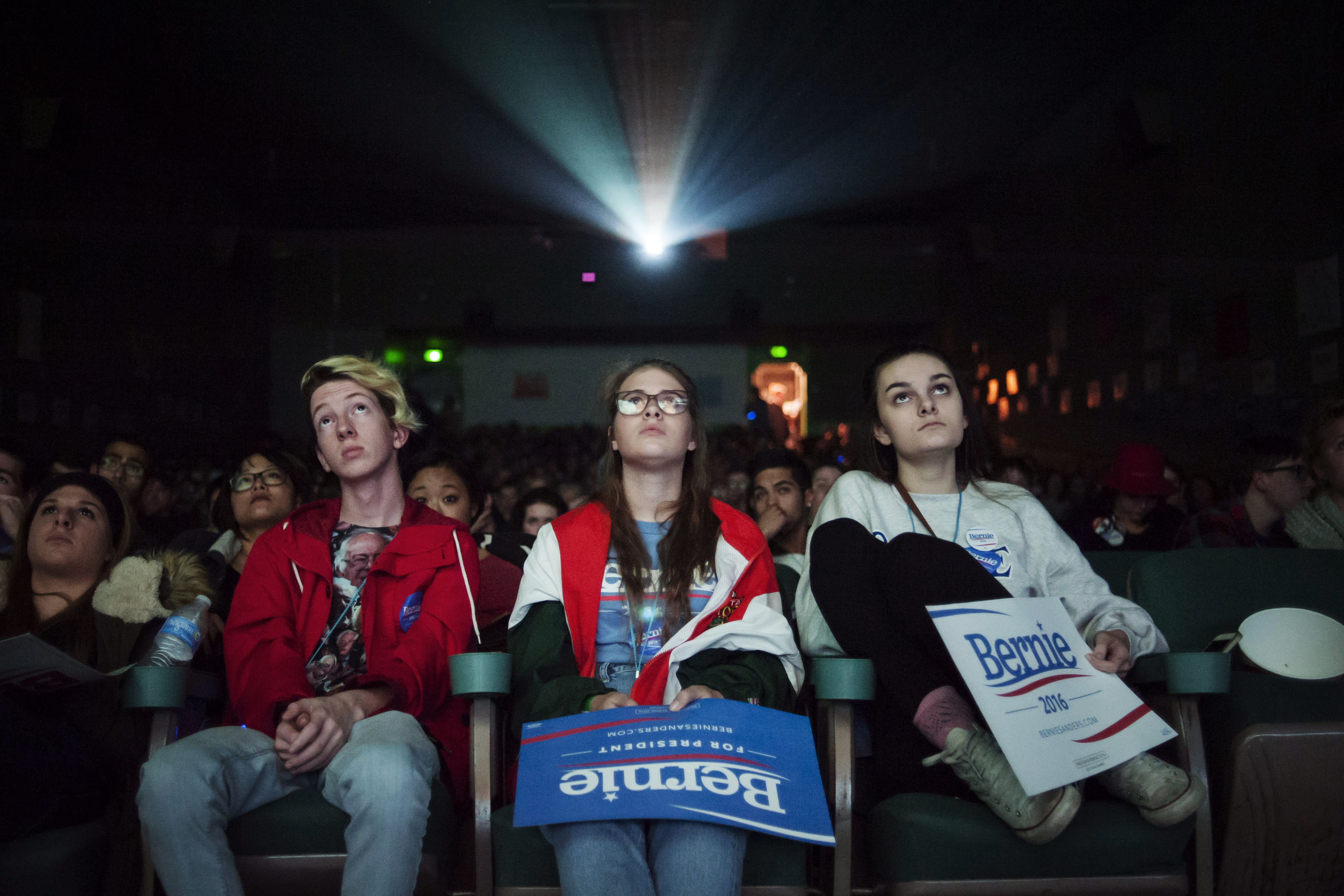 Jonah Guy, Deni Baird, and Lenin Cardwell watch a debate on a movie screen during a watch event in support of Democratic presidential candidate, Vermont Sen. Bernie Sanders in Des Moines, Iowa on Nov. 14, 2015.