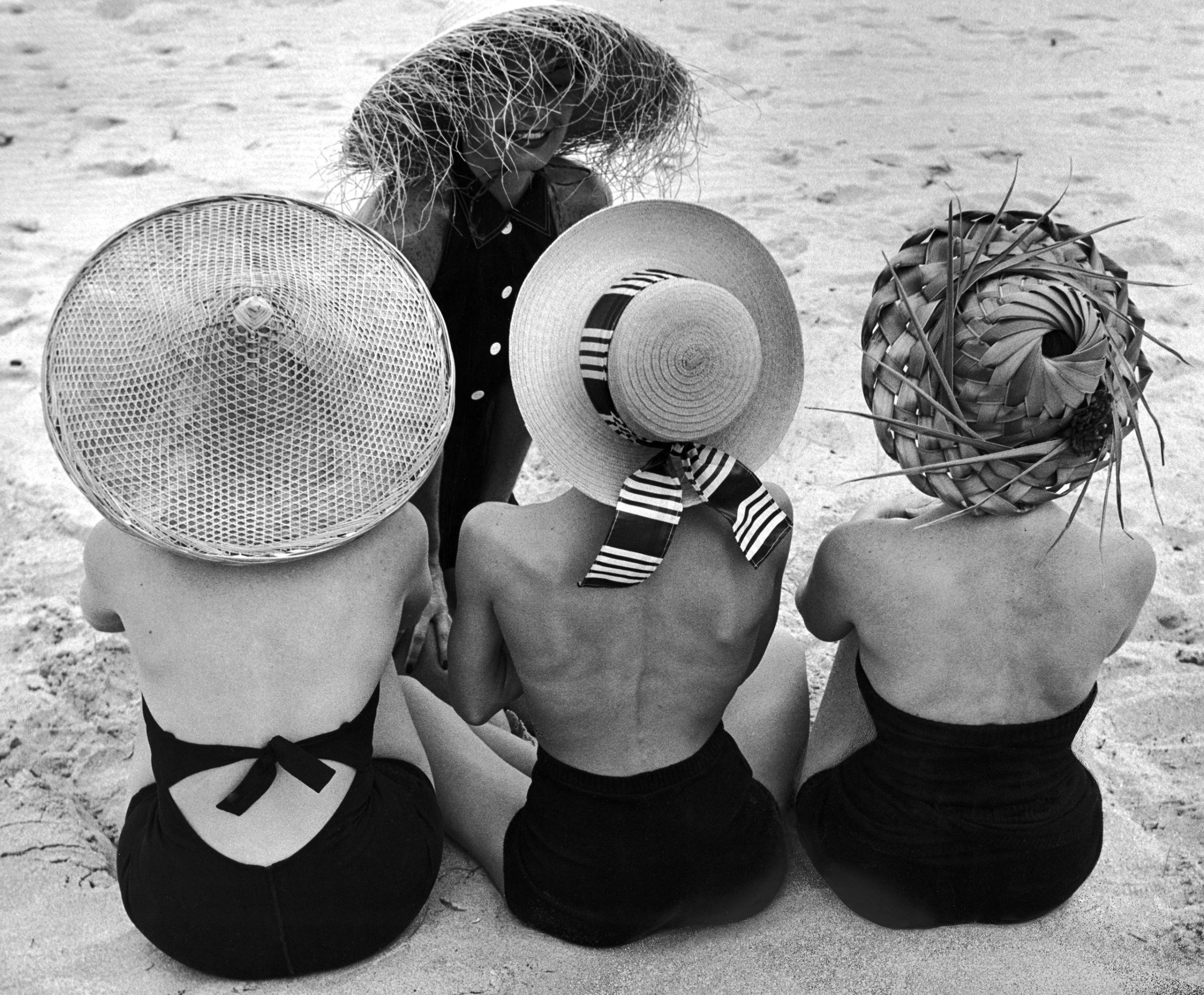 Models on beach wearing different designs of straw hats. 1950.