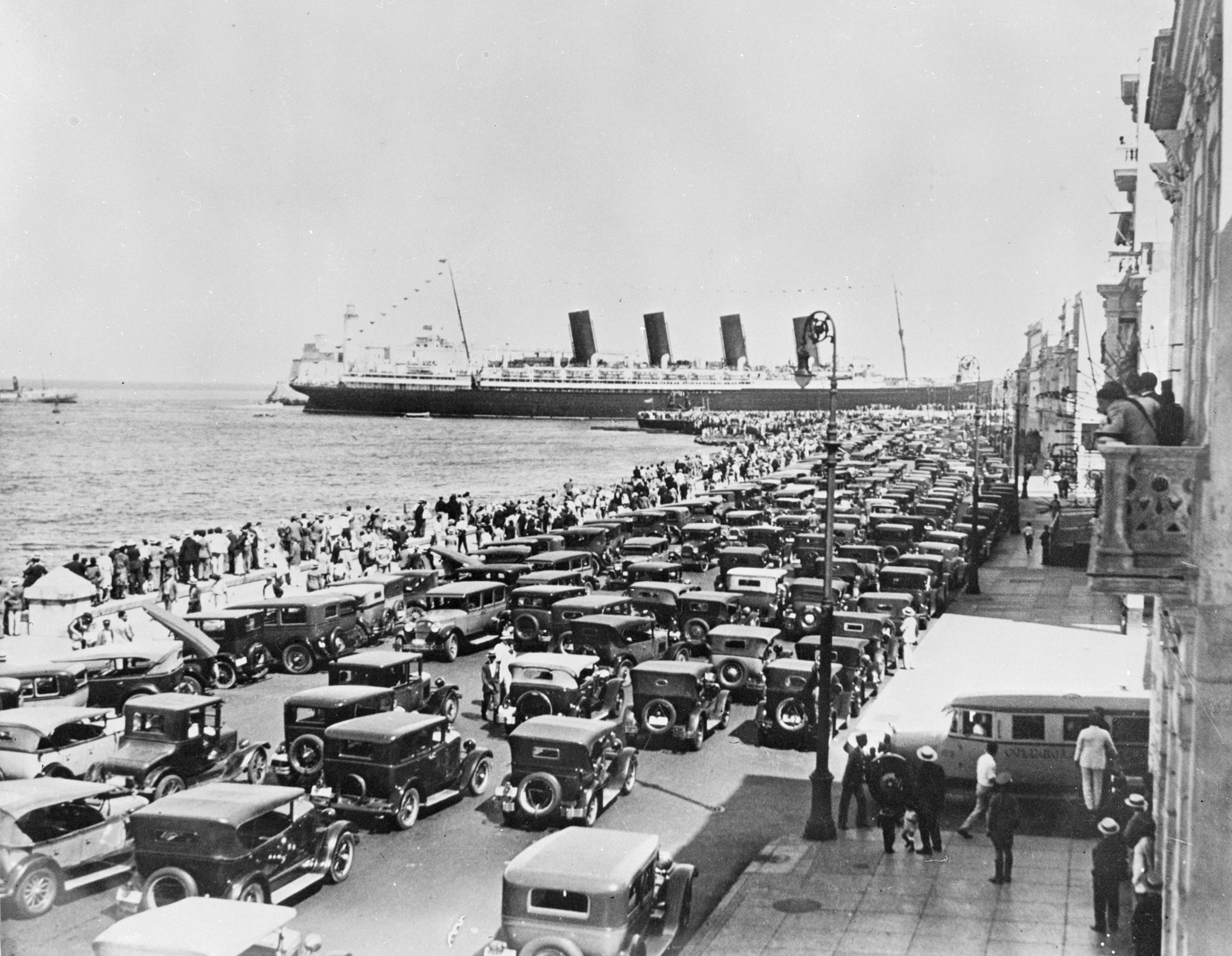 Hordes of people and motor cars crowd the waterfront as the Cunard liner Mauretania pulls into Havana, Cuba. 1925.