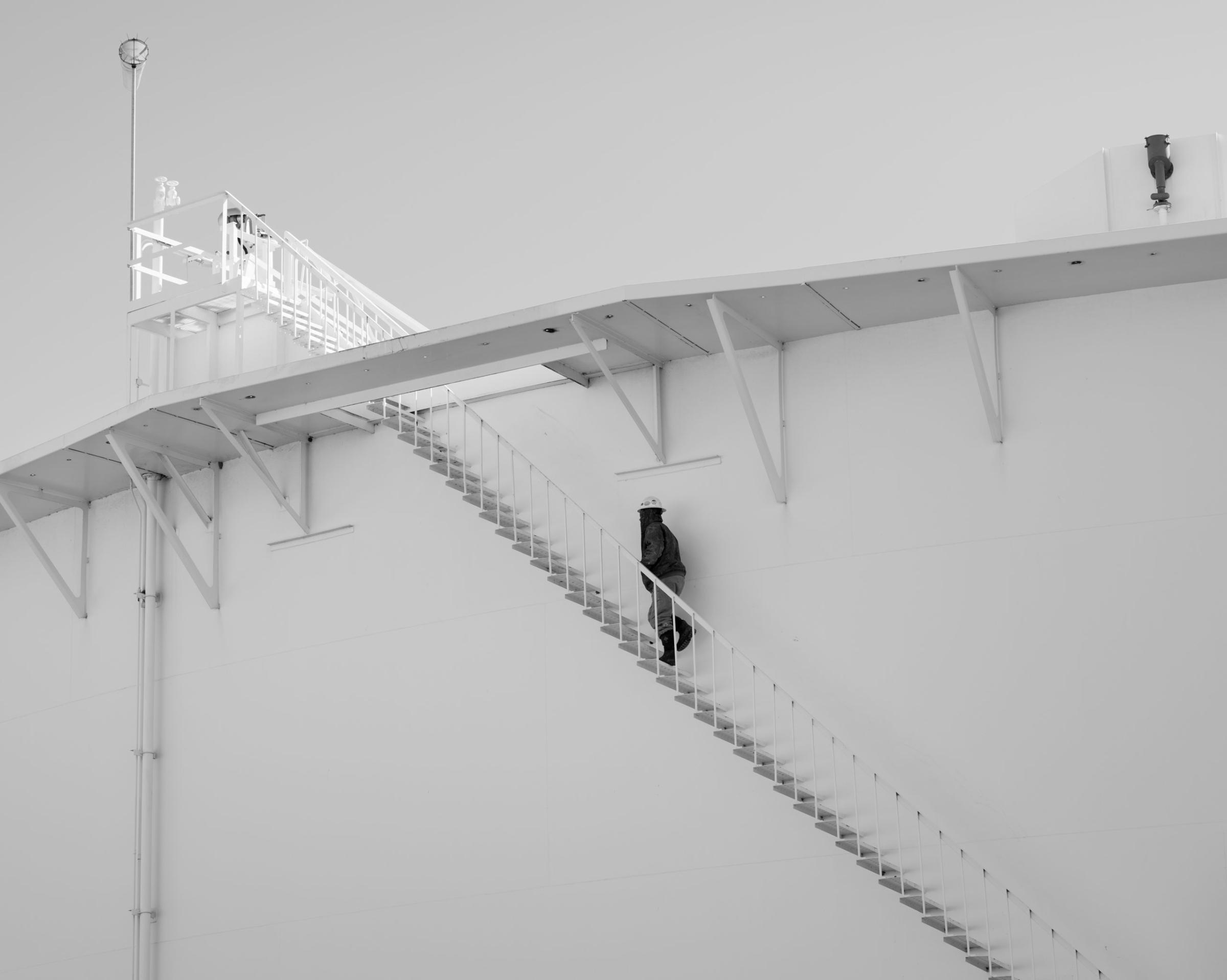 A worker walks up stairs on an oil storage tank, Cushing, Oklahoma. Cushing is a vital transshipment point with many intersecting pipelines, storage facilities and easy access to refiners and suppliers. Crude oil flows inbound to Cushing from all directions and outbound through dozens of pipelines. It is one of the largest oil reserves in the world.