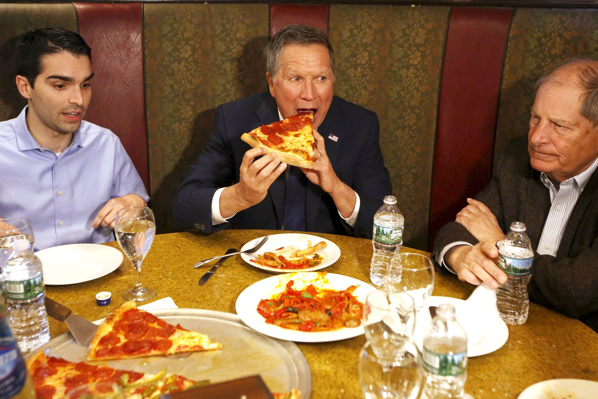 Republican presidential candidate, Ohio Gov. John Kasich eats a slice of pizza with Eric Ulrich, left, New York City Council member for the 32nd District of Queens, and former Congressman Bob Turner at Gino's Pizzeria and Restaurant in the Queens borough of New York on March 30, 2016.