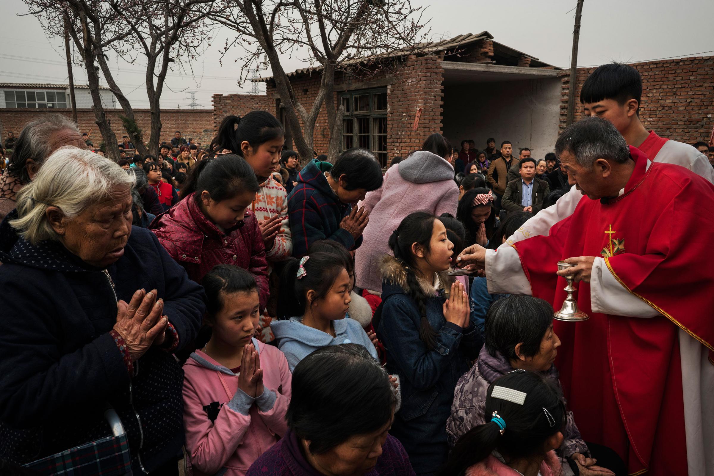 Villagers receive Communion from dissident Catholic Priest Dong Baolu at an underground Palm Sunday service in the yard of a house in Youtong village, Shijiazhuang, China, March 20, 2016.