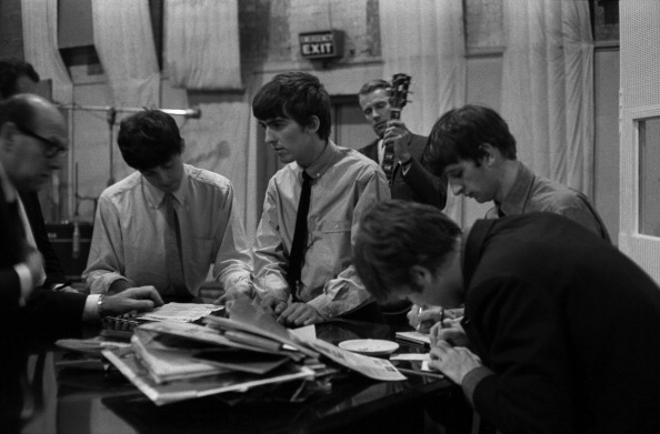 The Beatles sign documents for music publisher Dick James in Studio 2 at Abbey Road in London recording the single 'She Loves You', 1st July 1963, L-R Dick James, Paul McCartney, George Harrison, producer George Martin (in background), John Lennon (writing) and Ringo Starr. (Terry O'Neill—Getty Images)