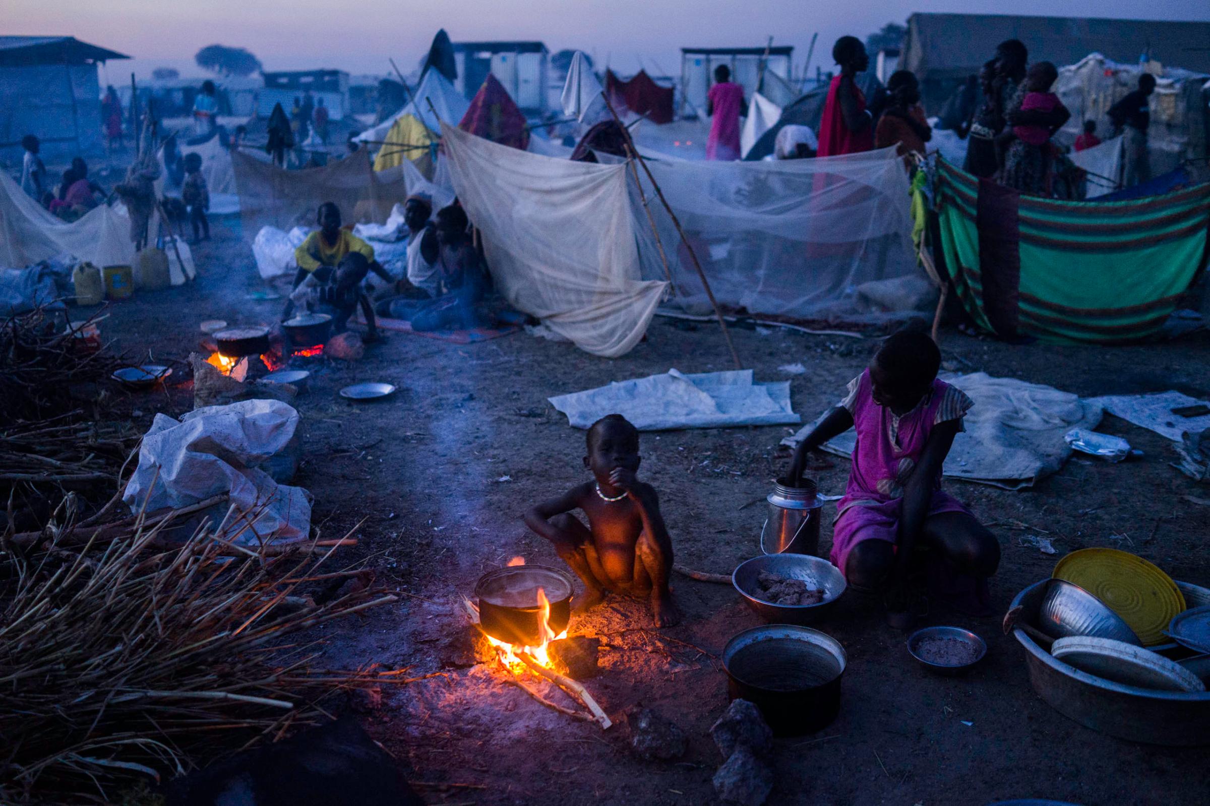 A mother prepares food for her child at a United Nations camp, where more than 100,00 displaced people seek security and food, in Bentiu, People walk past a drainage ditch in the United Nations camp in Bentiu, Unity State, South Sudan.