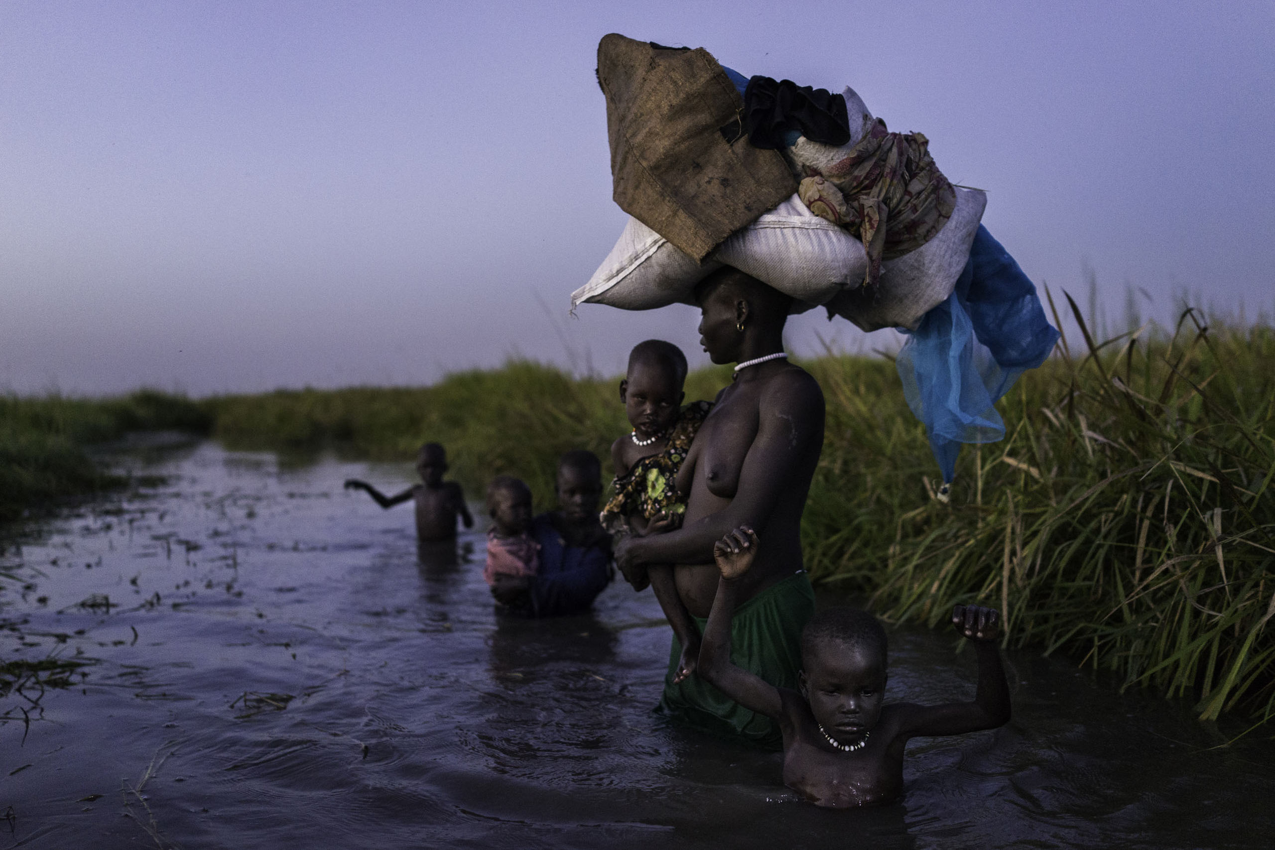 After receiving food at a distribution site, a woman and her five children walk through the cold swamps at dusk to her hiding place on Kok Island, Unity State, South Sudan.