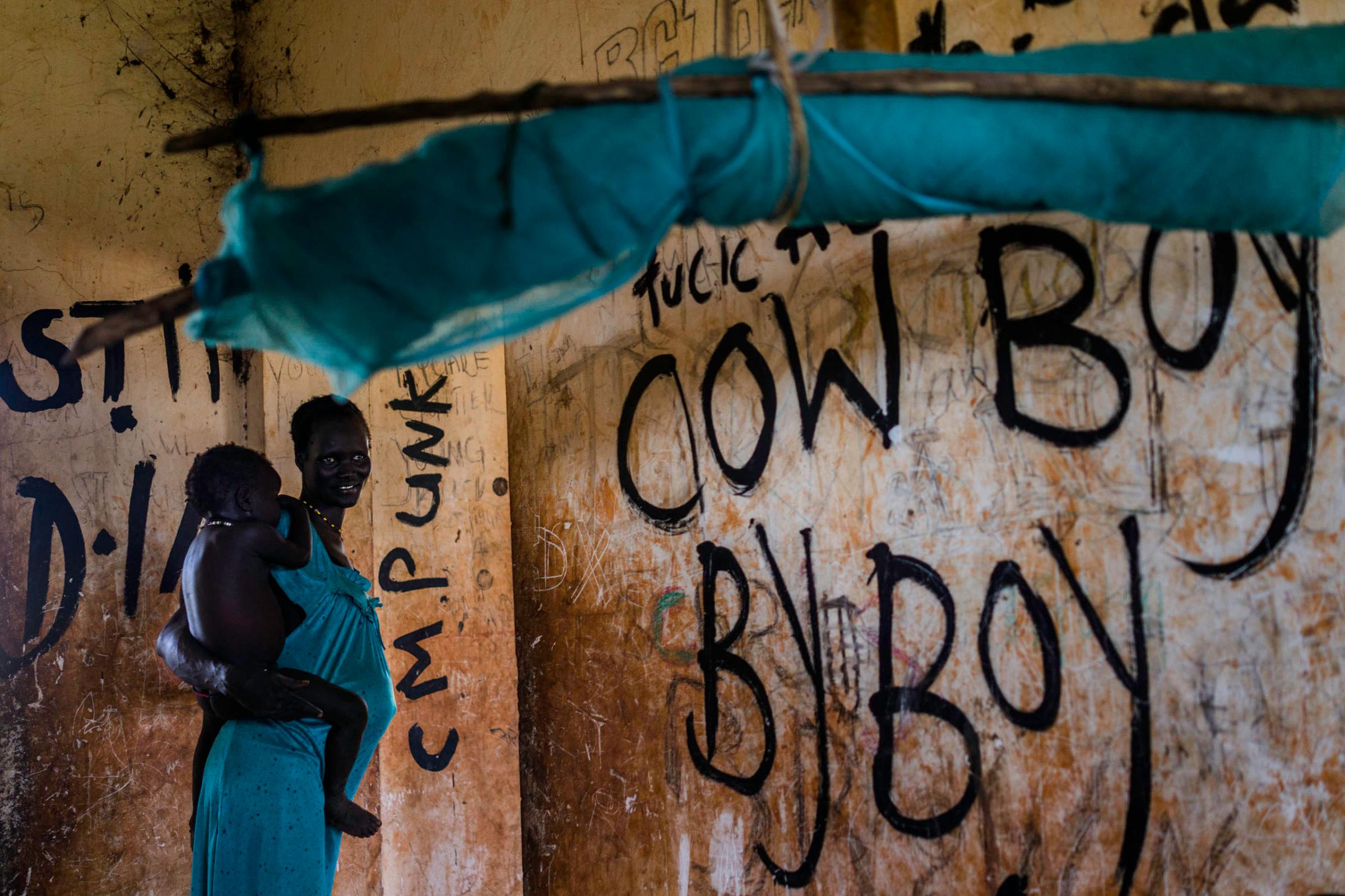 A mother holds her baby inside an abandoned building covered in graffiti, where over a dozen families have sought refuge from fighting, in Bentiu, Unity State, South Sudan.