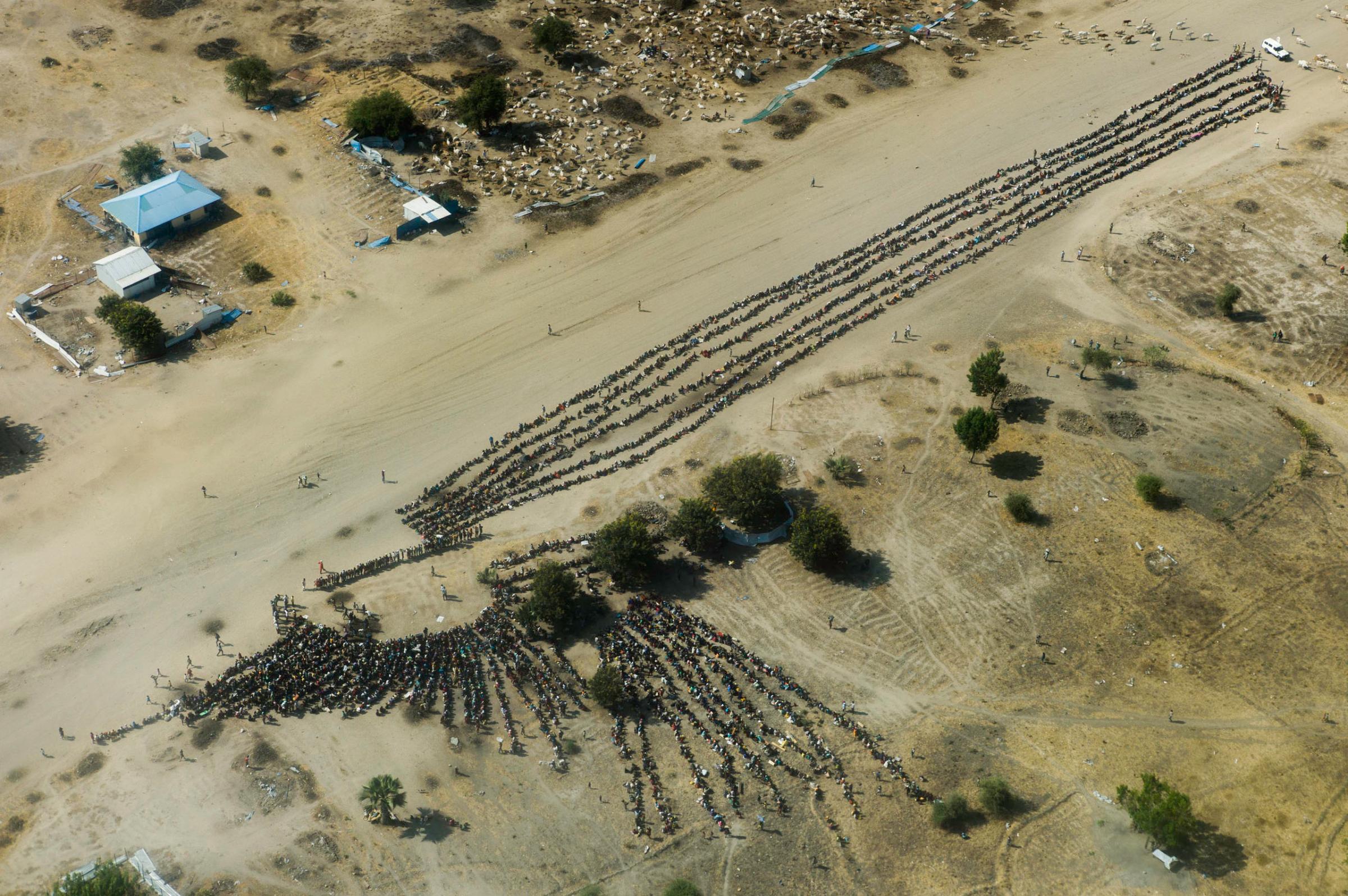 An aerial view of thousands of people waiting in line for food distribution in the otherwise empty and destroyed town of Leer, Unity State, South Sudan.