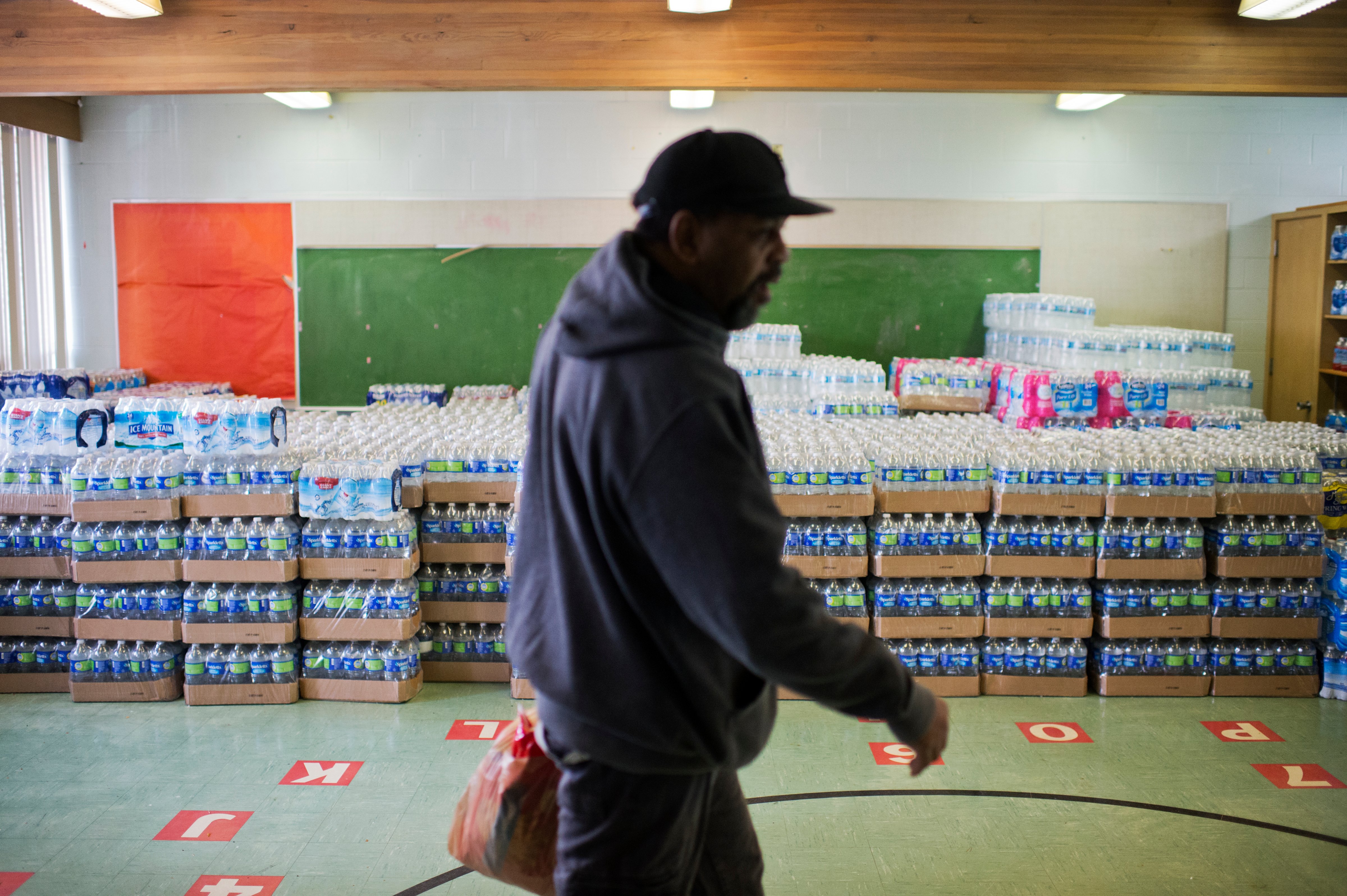 UNITED STATES - FEBRUARY 23: A volunteer walks by cases of bottled water at the St. Mark Baptist Church in Flint, Mich., that serves as a water distribution area, February 23, 2016. The water supply was not properly treated after being switched from Lake Huron to the Flint River and now contains lead and iron. (Photo By Tom Williams/CQ Roll Call)