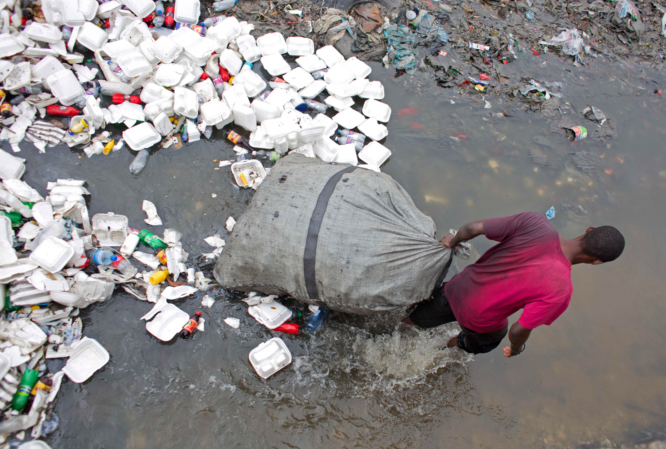 In this Feb. 28, 2016 photo, man wades through a garbage filled water canal pulling his bag after collecting empty bottles to sell, in downtown of Port-au-Prince, Haiti. Scientists believe cholera was introduced to the country's biggest river by inadequately treated sewage from a base of U.N. peacekeepers. Victims' advocates have sued the U.N. in the United States, and a federal judge ruled last year that the organization was immune from a lawsuit seeking compensation. The U.S. Court of Appeals heard arguments in March 2016 for the plaintiffs challenging U.N. immunity claims, but a decision is not expected for months. (AP Photo/Dieu Nalio Chery)