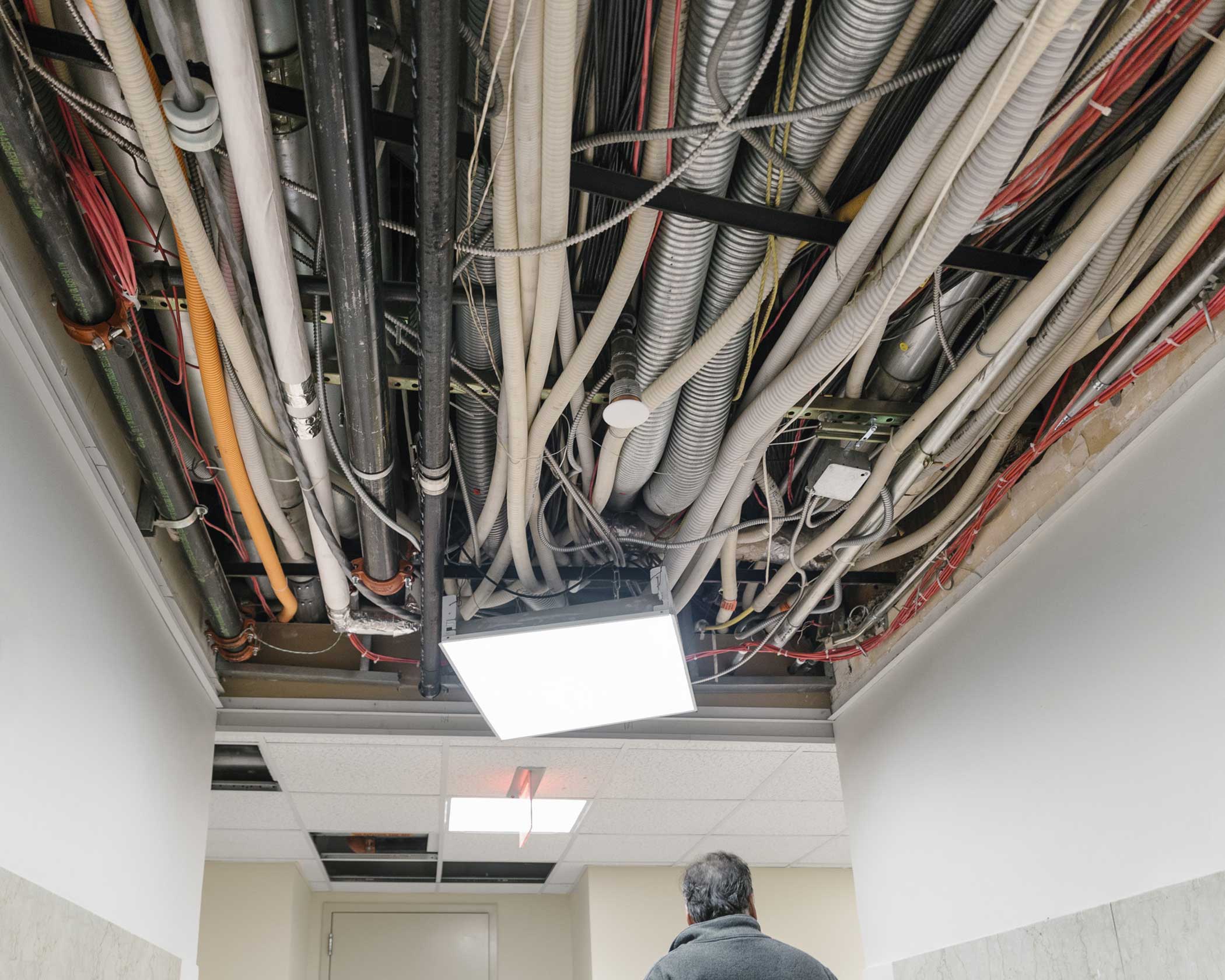 Ceiling tiles removed for maintenance reveal fiber cabling and utility lines.