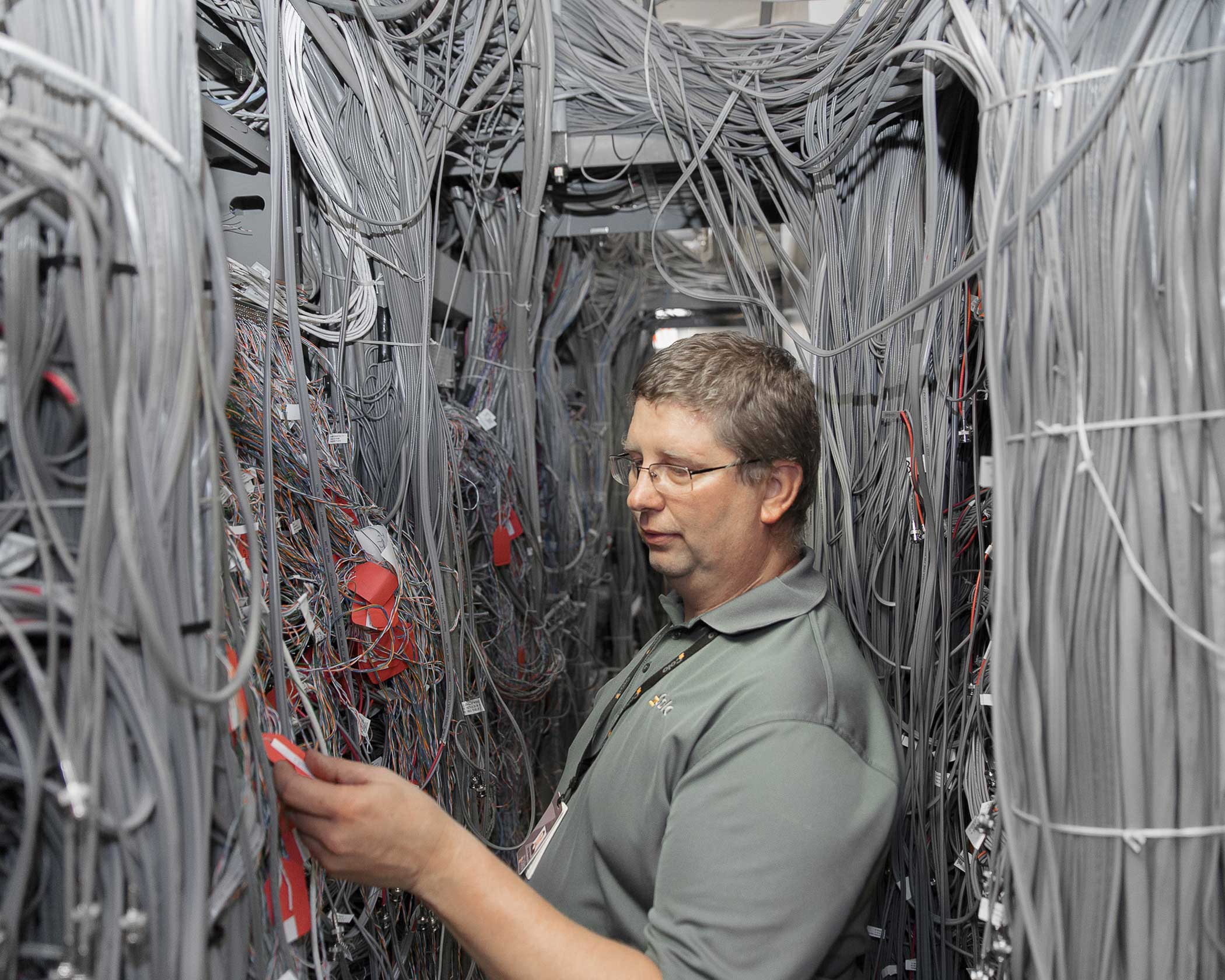 Copper cables form a dense mesh around a technician at 60 Hudson in a concentrated central hub aptly dubbed  The Nest.   Beneath the grey housing each cable is color coded and labeled to indicate its function.