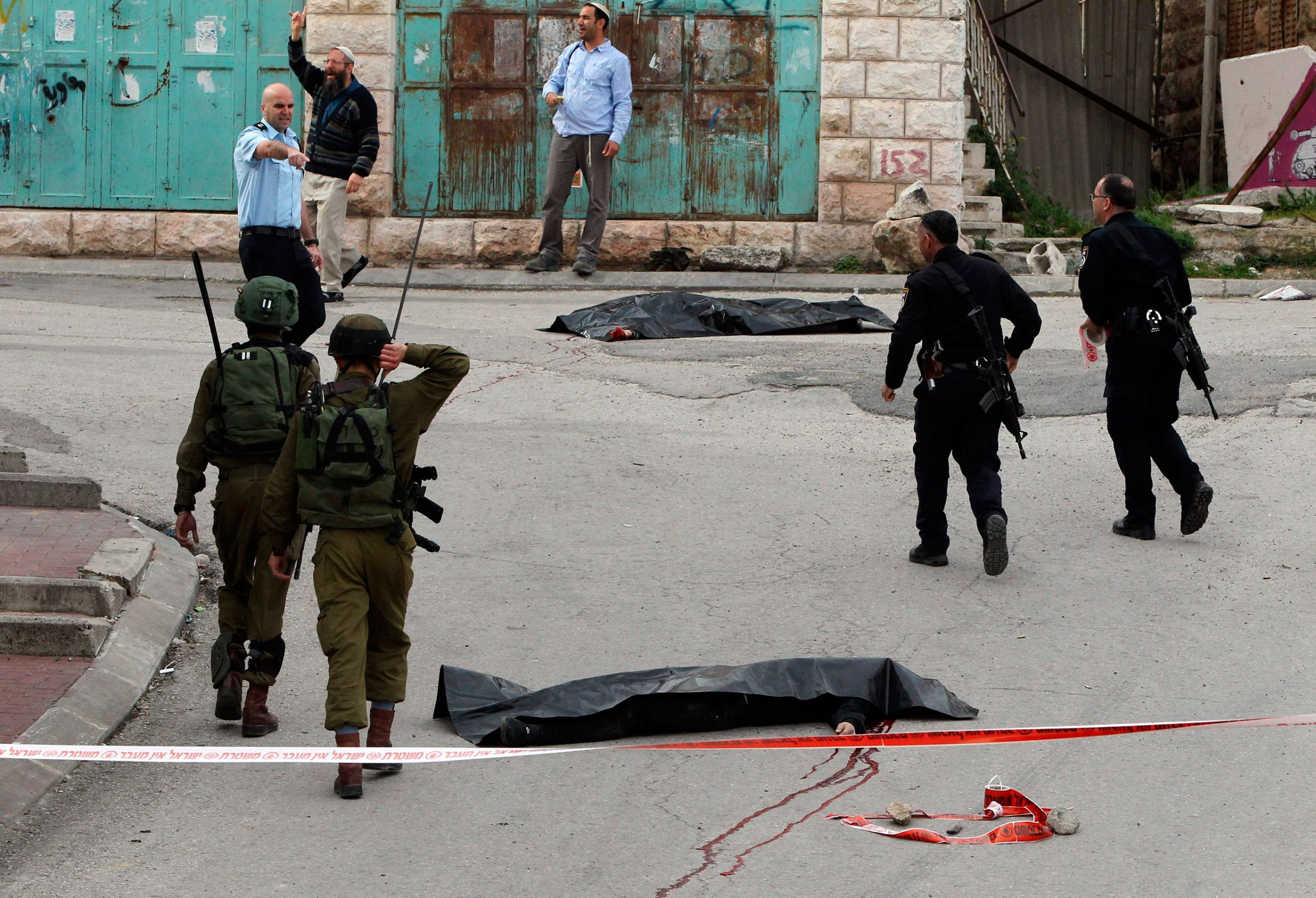 Israeli soldiers and police officers walk near the bodies of two Palestinians who were killed after wounding an Israeli soldier in a knife attack, before being shot dead by troops, in Hebron, West bank, March 24, 2016.