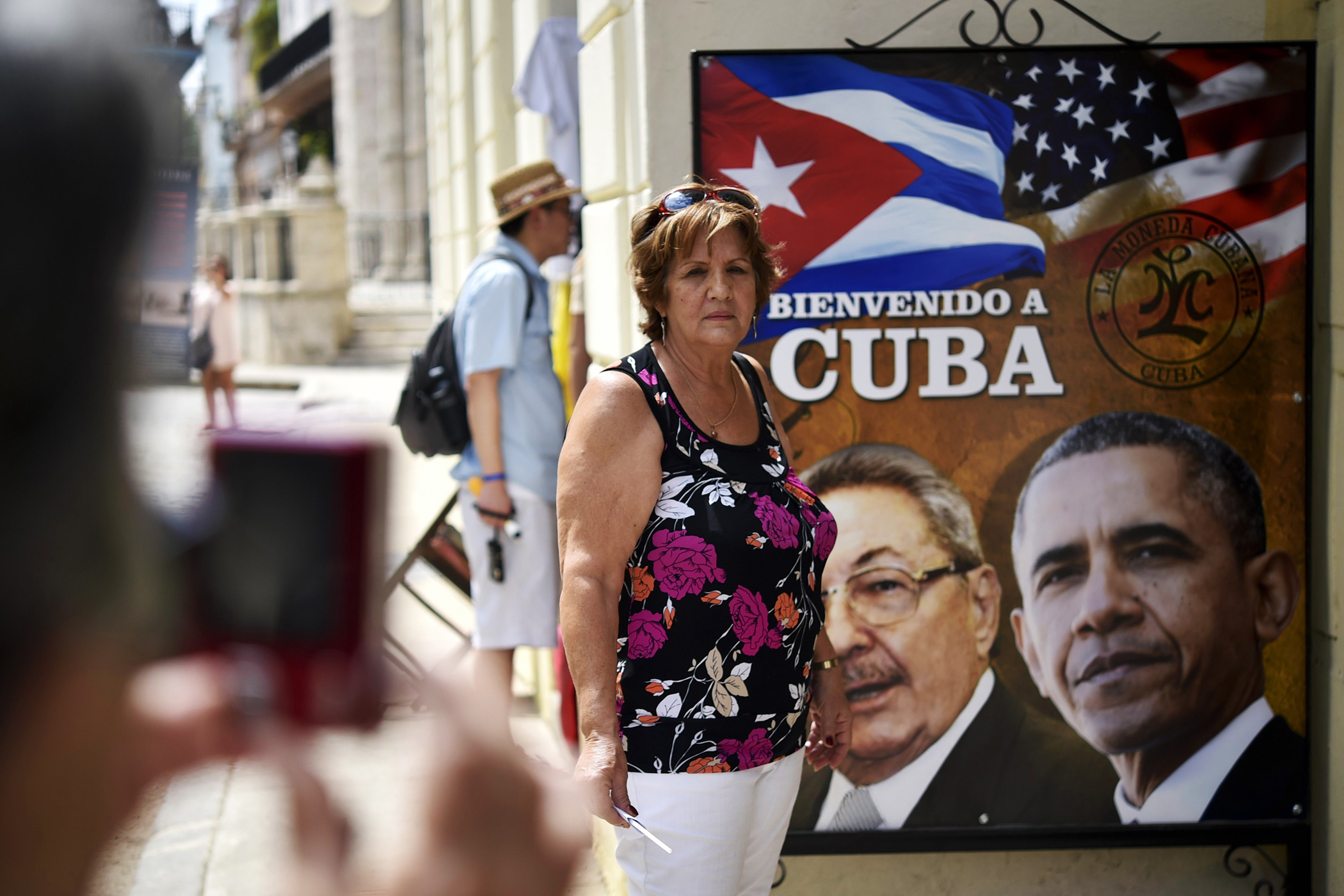 A Cuban woman poses for a picture with a sign displaying images of Cuban and U.S. Presidents Raul Castro and Barack Obama in Havana on March 19, 2016.