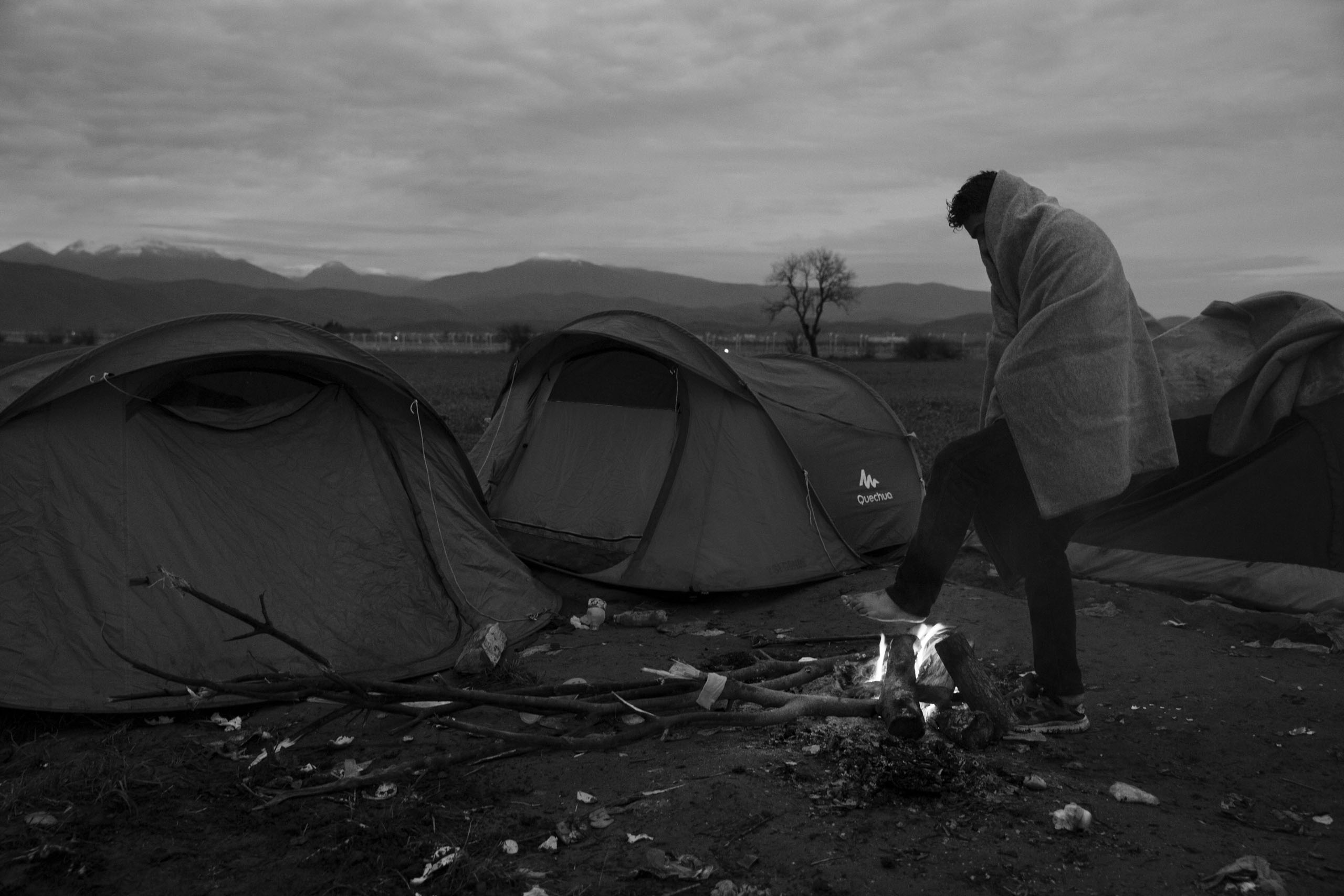 A man warms his feet at a sprawling refugee camp along the border of Greece and Macedonia near the town of Idomeni. The refugees are being stopped from moving beyond Greece and have been languishing in the rain, mud, and cold with insufficient food and medical care while sleeping in  small tents, March 12, 2016