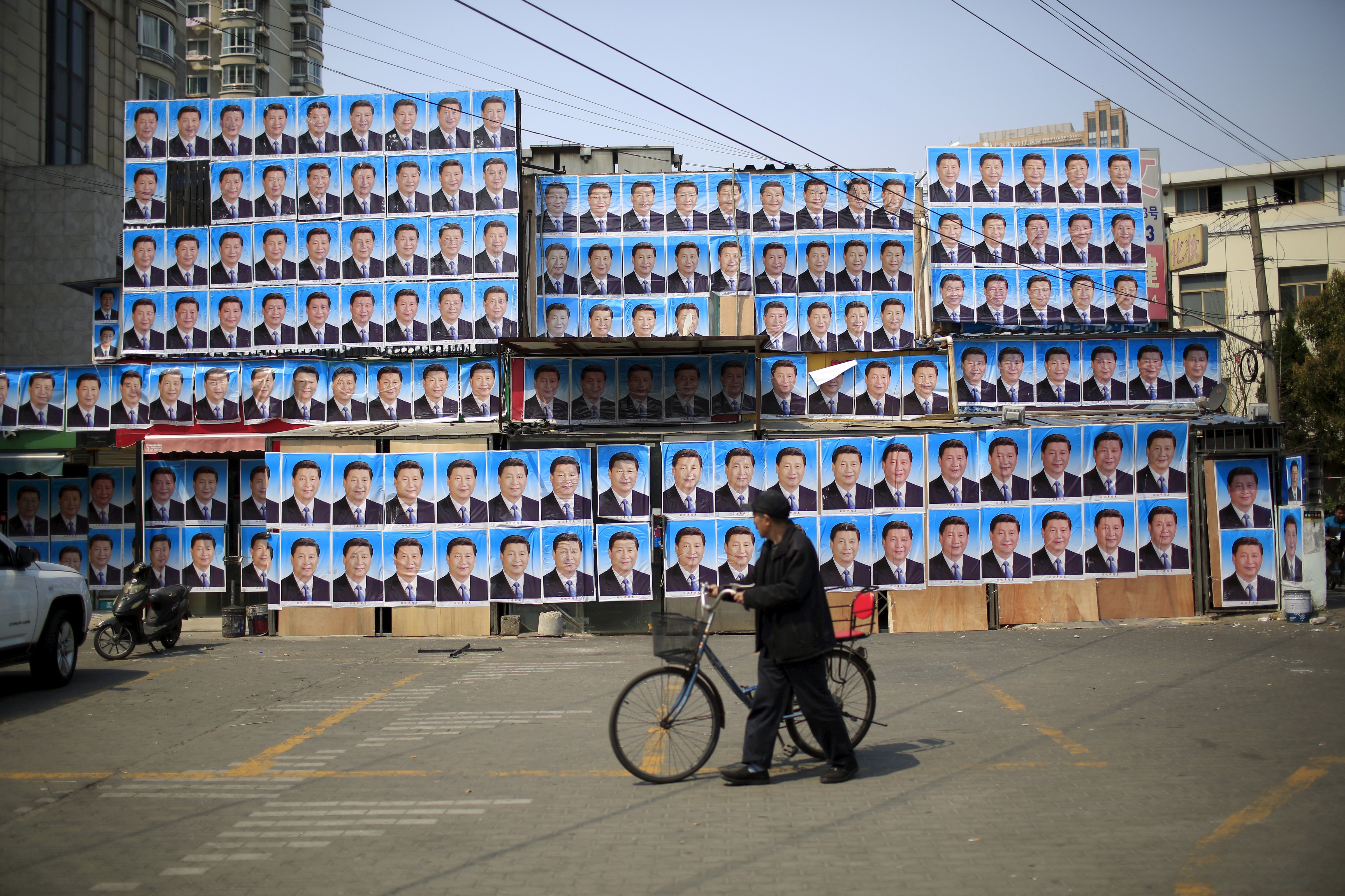 A man with a bicycle walks past a building covered in posters of Chinese President Xi Jinping in Shanghai