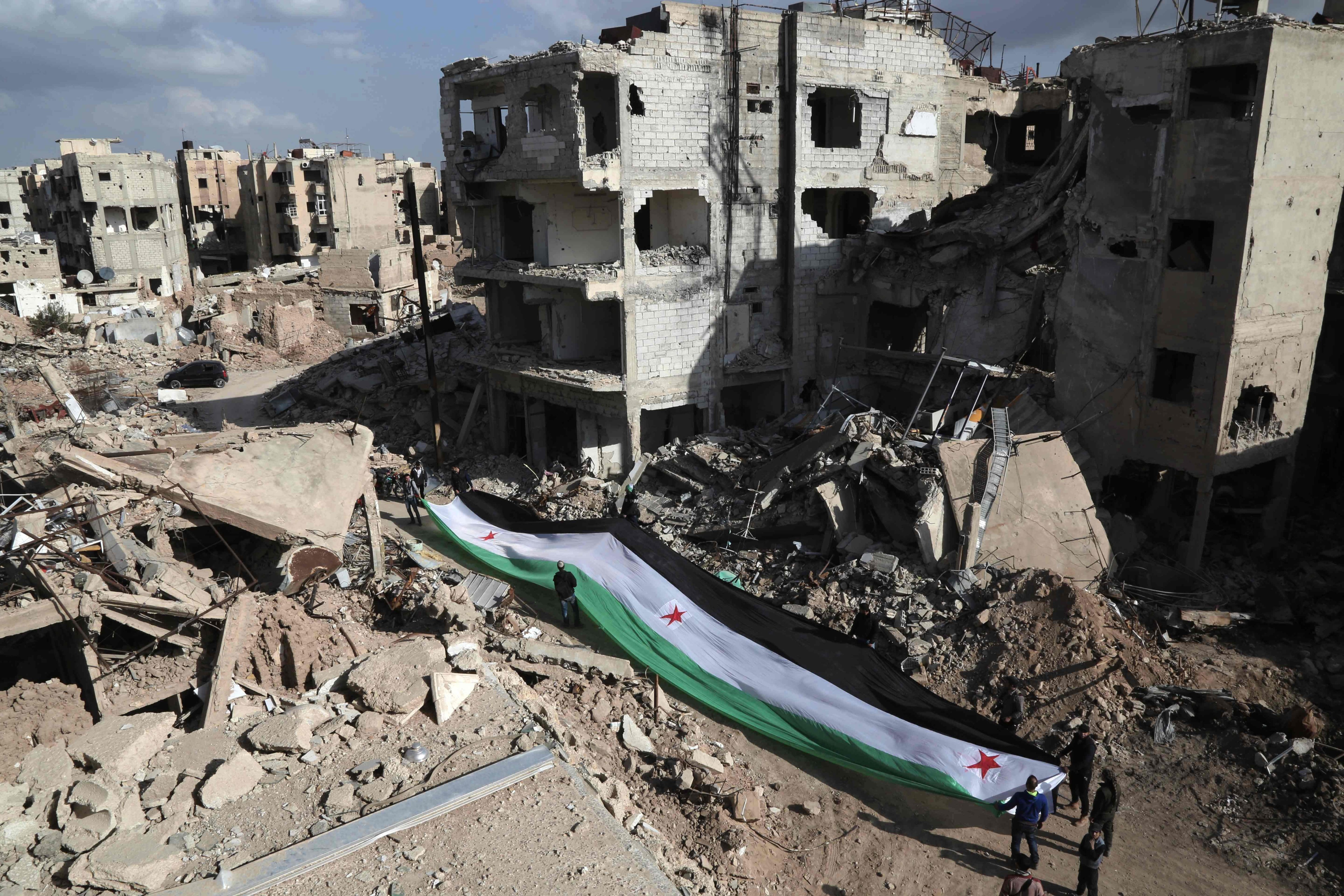 Residents and activists hold a giant pre-Baath Syrian flag, now used by the Syrian opposition, during an anti-regime protest in the rubble of destroyed buildings in the neighbourhood of Jobar, on the eastern outskirts of the capital Damascus, on March 3, 2016. (Amer Almohibany—AFP/Getty Images)
