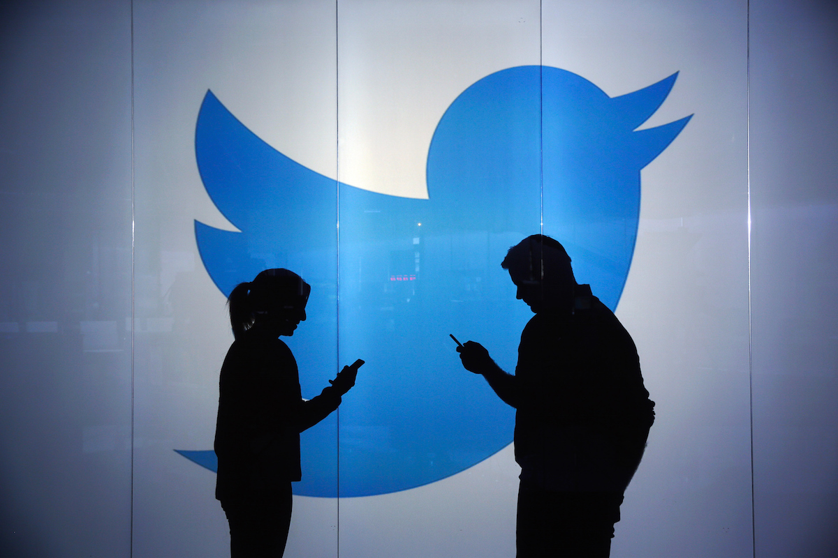 People check mobile devices whilst standing against an illuminated wall bearing Twitter Inc.'s logo in this arranged photograph in London on Jan. 5, 2016. (Chris Ratcliffe—Bloomberg / Getty Images)
