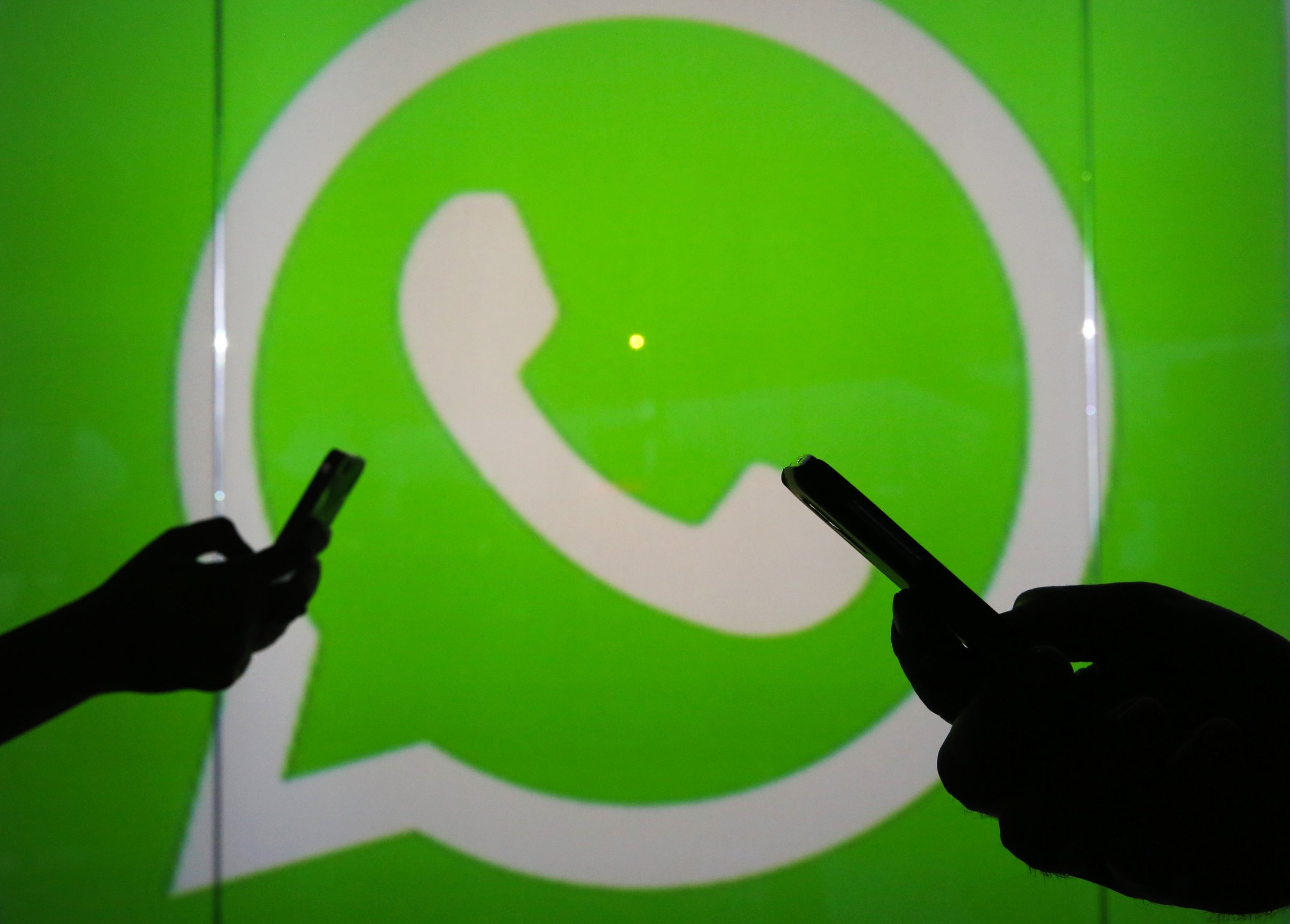 People are seen as silhouettes as they check mobile devices whilst standing against an illuminated wall bearing WhatsApp Inc's logo in this arranged photograph in London, U.K., on Tuesday, Jan. 5, 2016