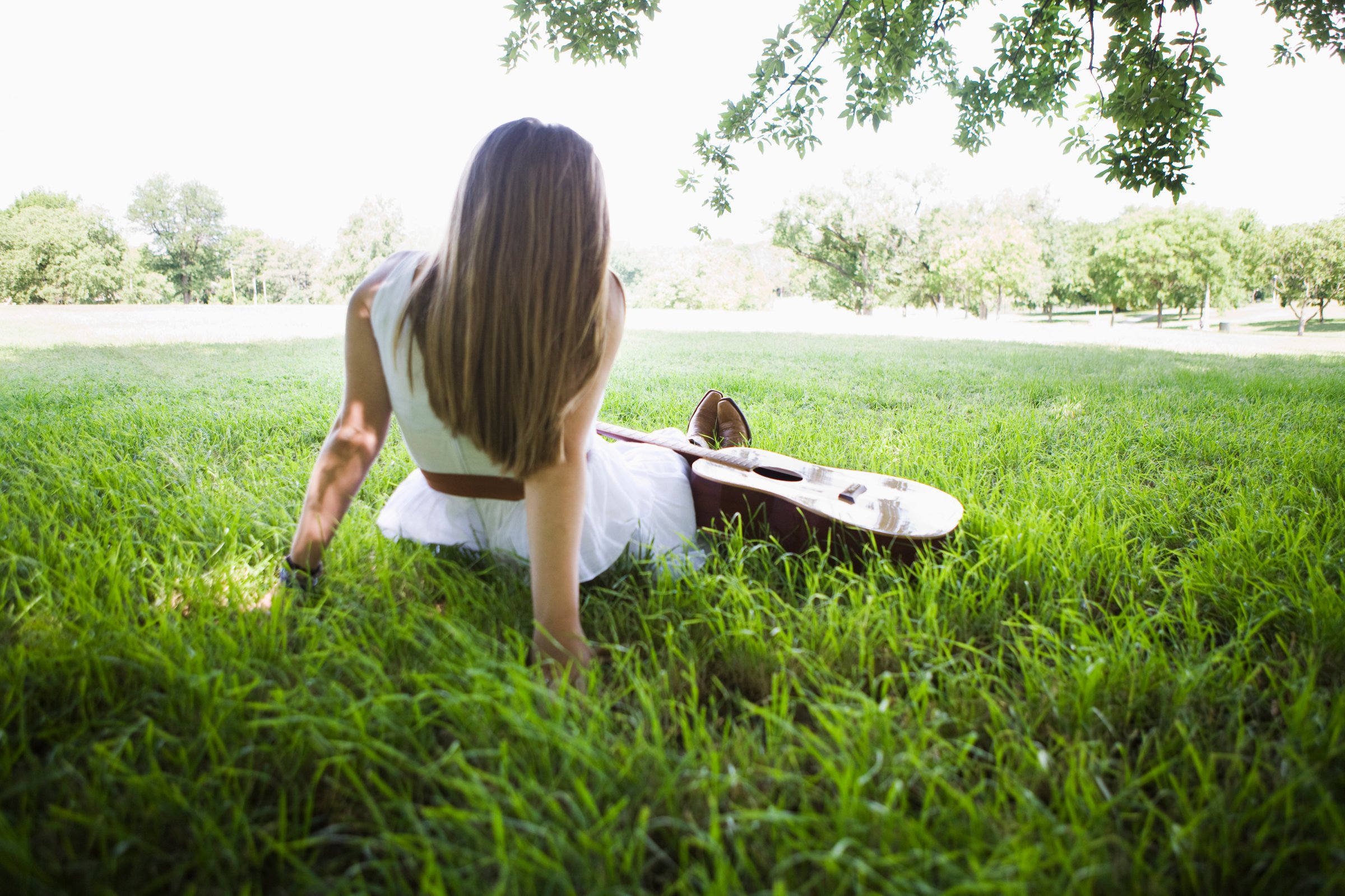 woman-sitting-grass-guitar-rear-view